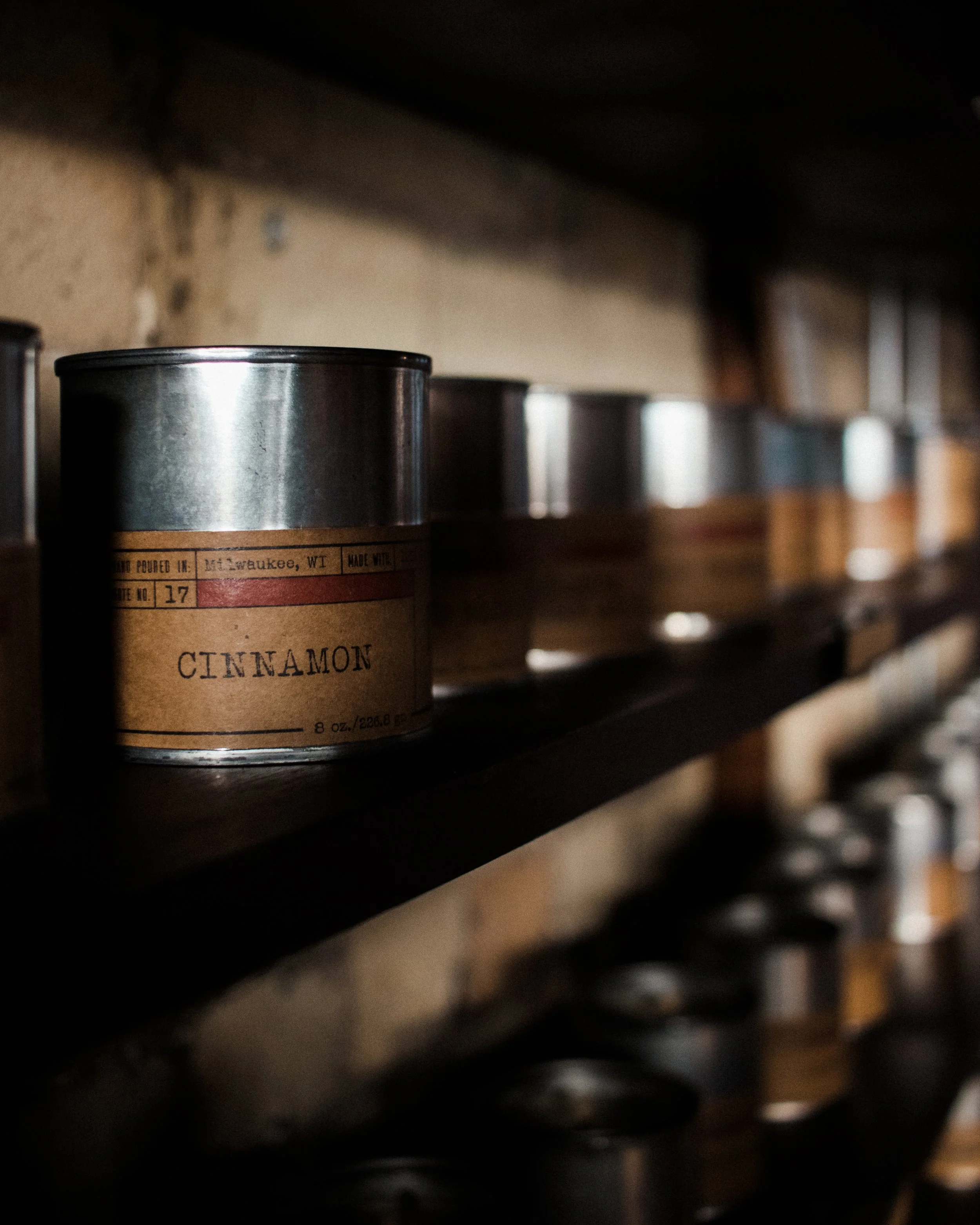 A row of scent shelf candles in metal tins line a shelf. 