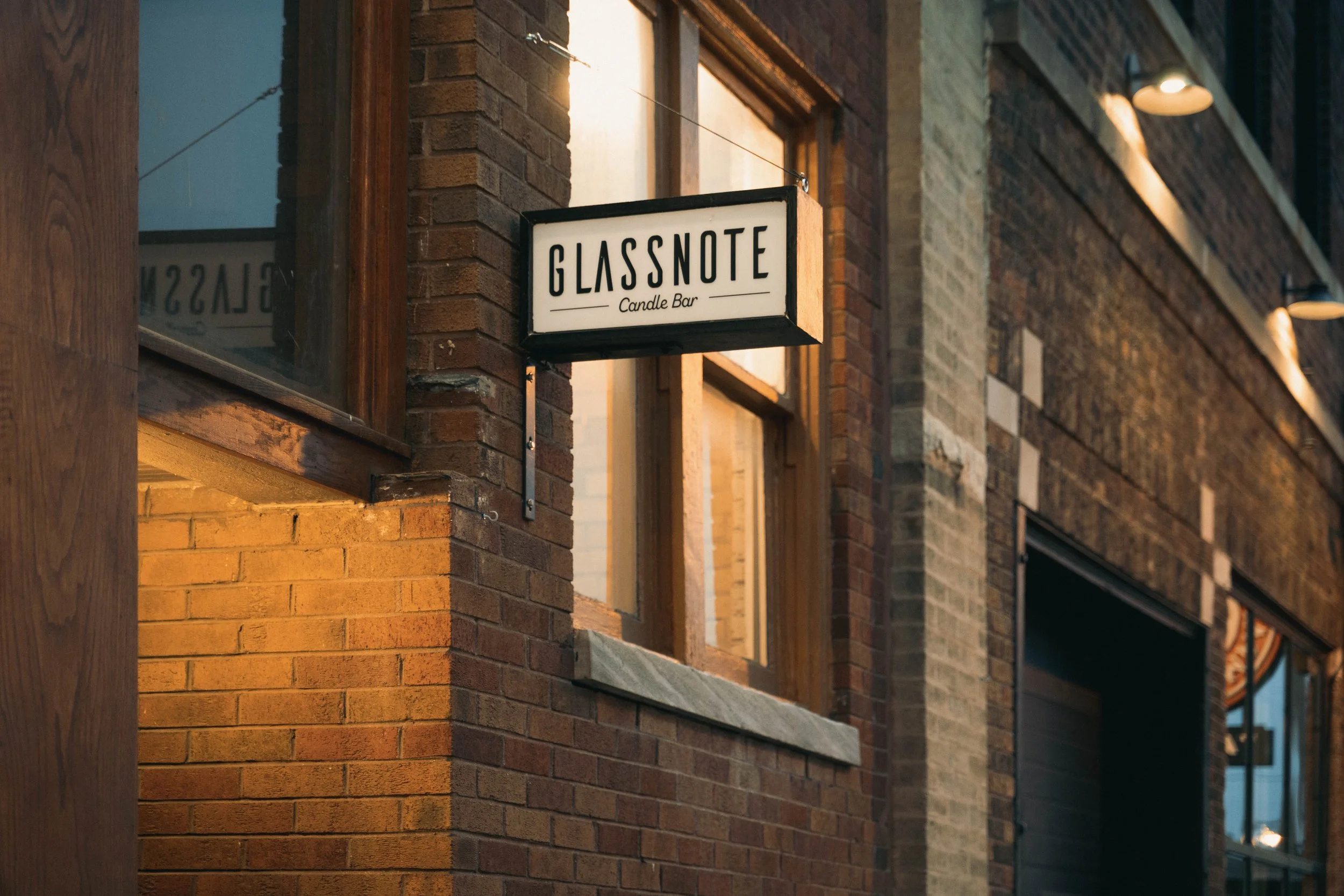 Signboard for Glassnote Candle Bar hanging on a brick building exterior with warm lighting.
