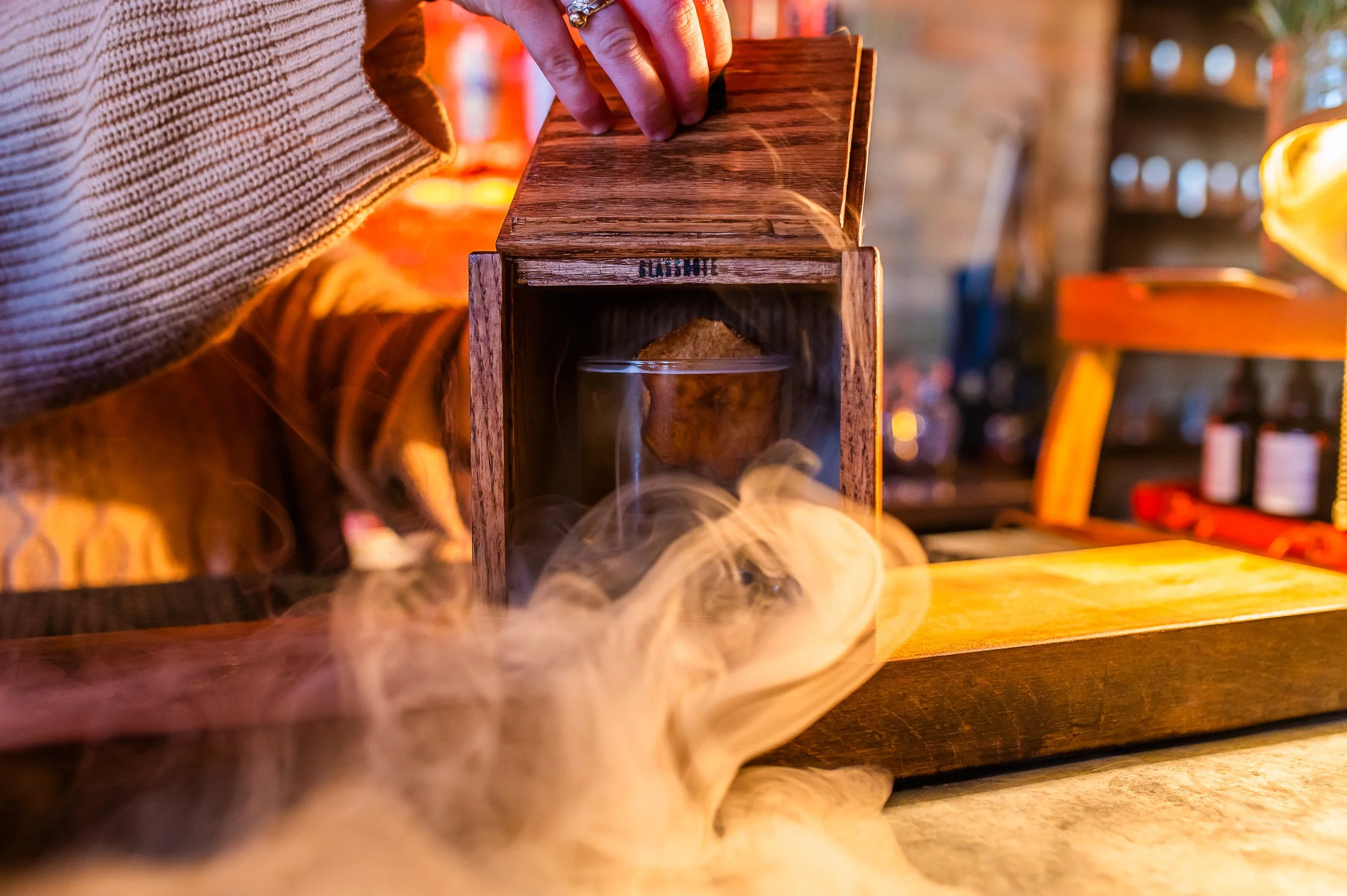 A person is opening a wooden box labeled 'GHOST' with a glass container inside, emitting smoke or vapor.