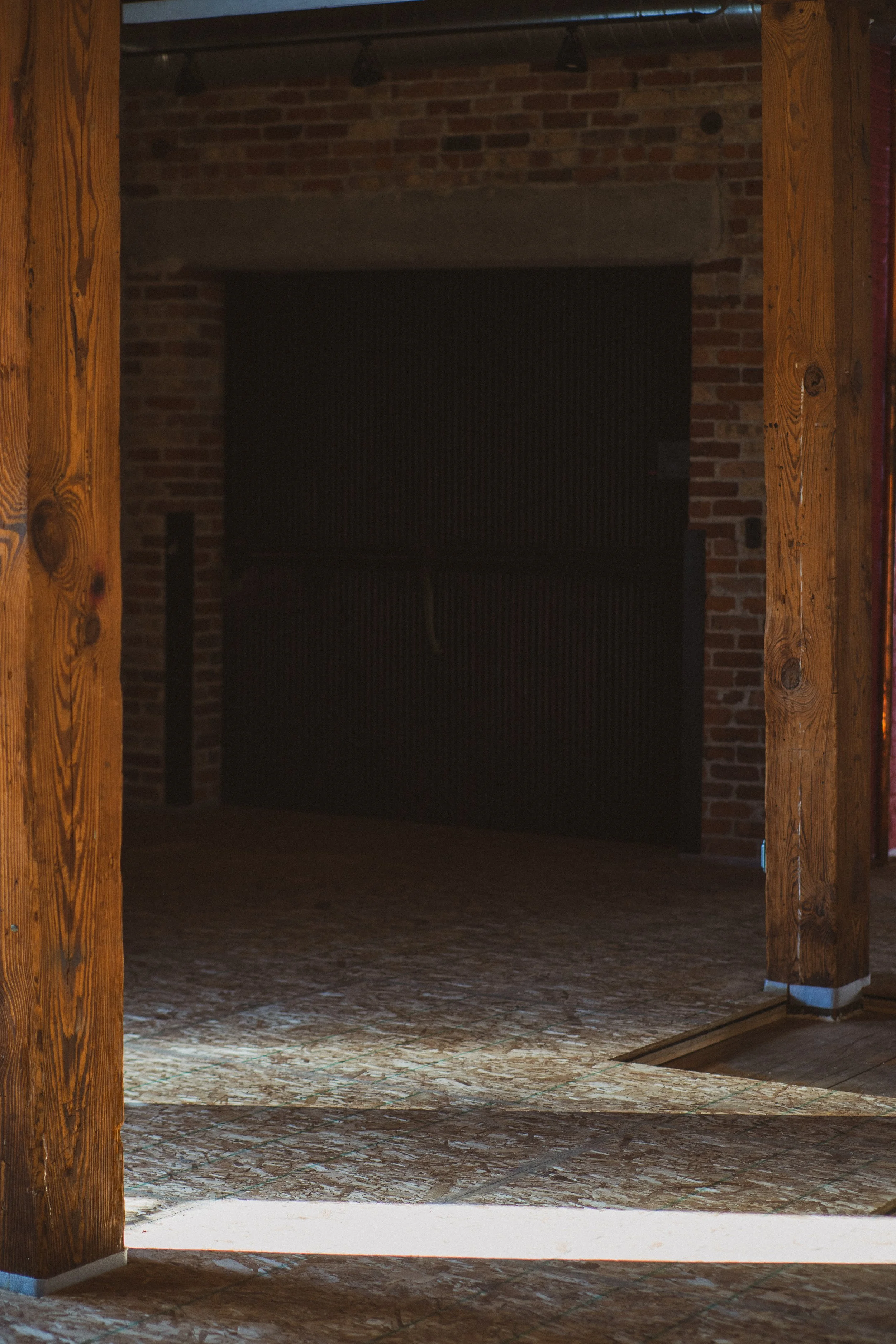 An interior of a rustic building with brick walls, wooden beams, and a freight elevator in the background, illuminated by sunlight.