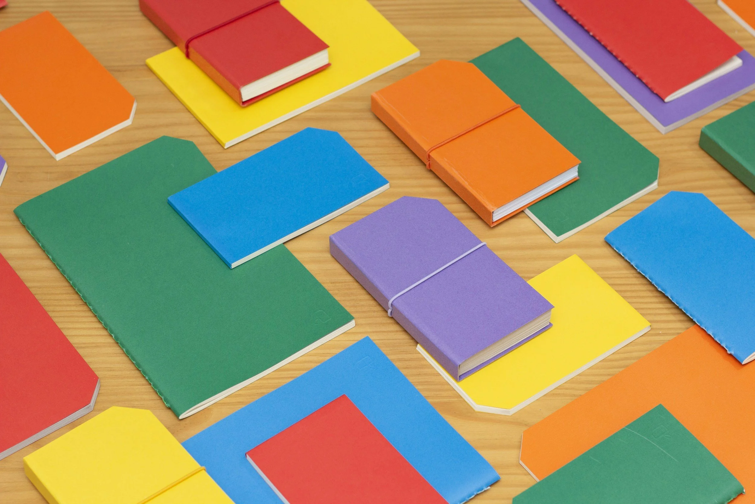 Bunte Notizbücher in verschiedenen Farben liegen auf einem Holztisch, einige sind mit Gummibändern zusammengebunden.