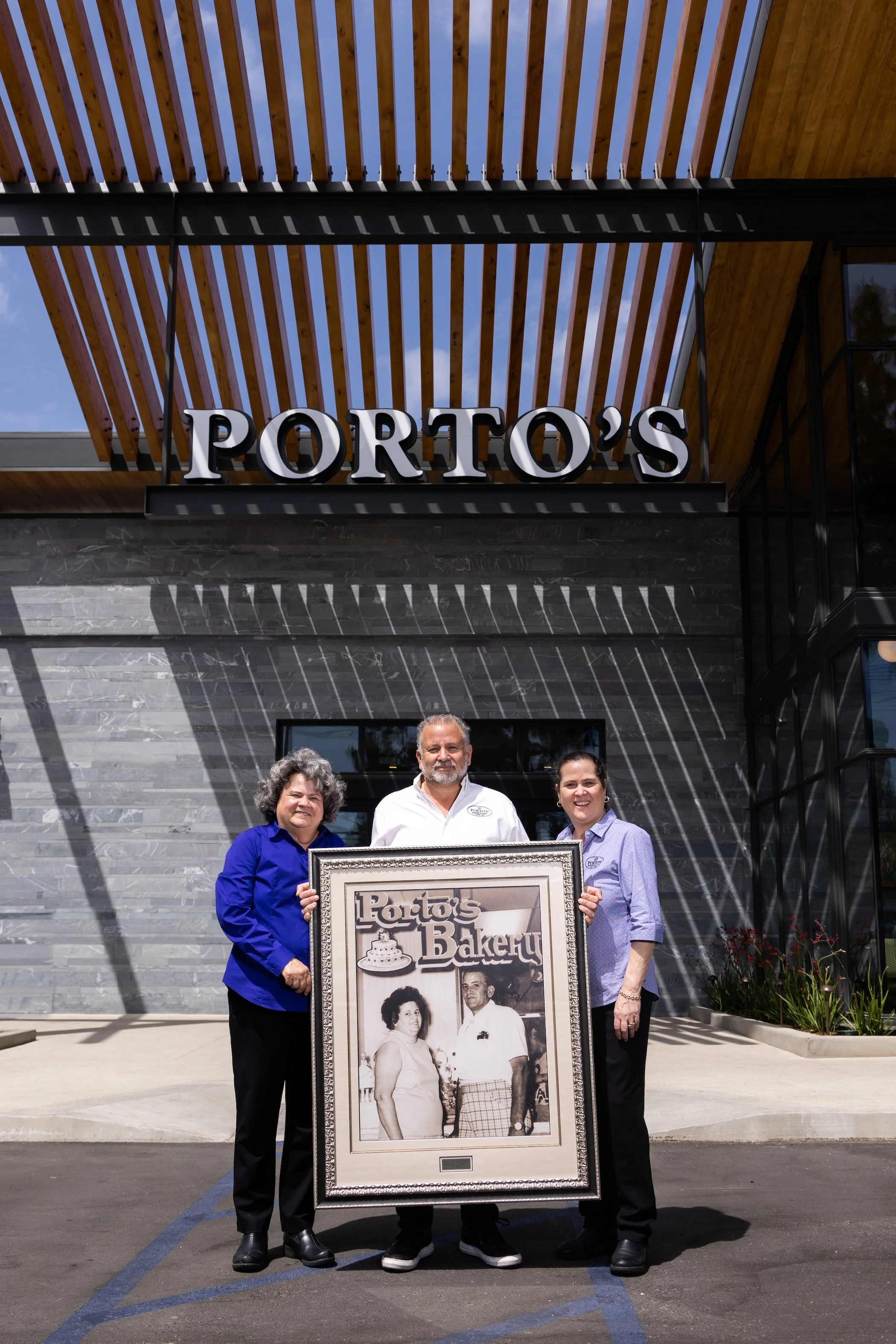 An image of the Porto family holding a black and white photo of Rosa in front of the Porto's Bakery