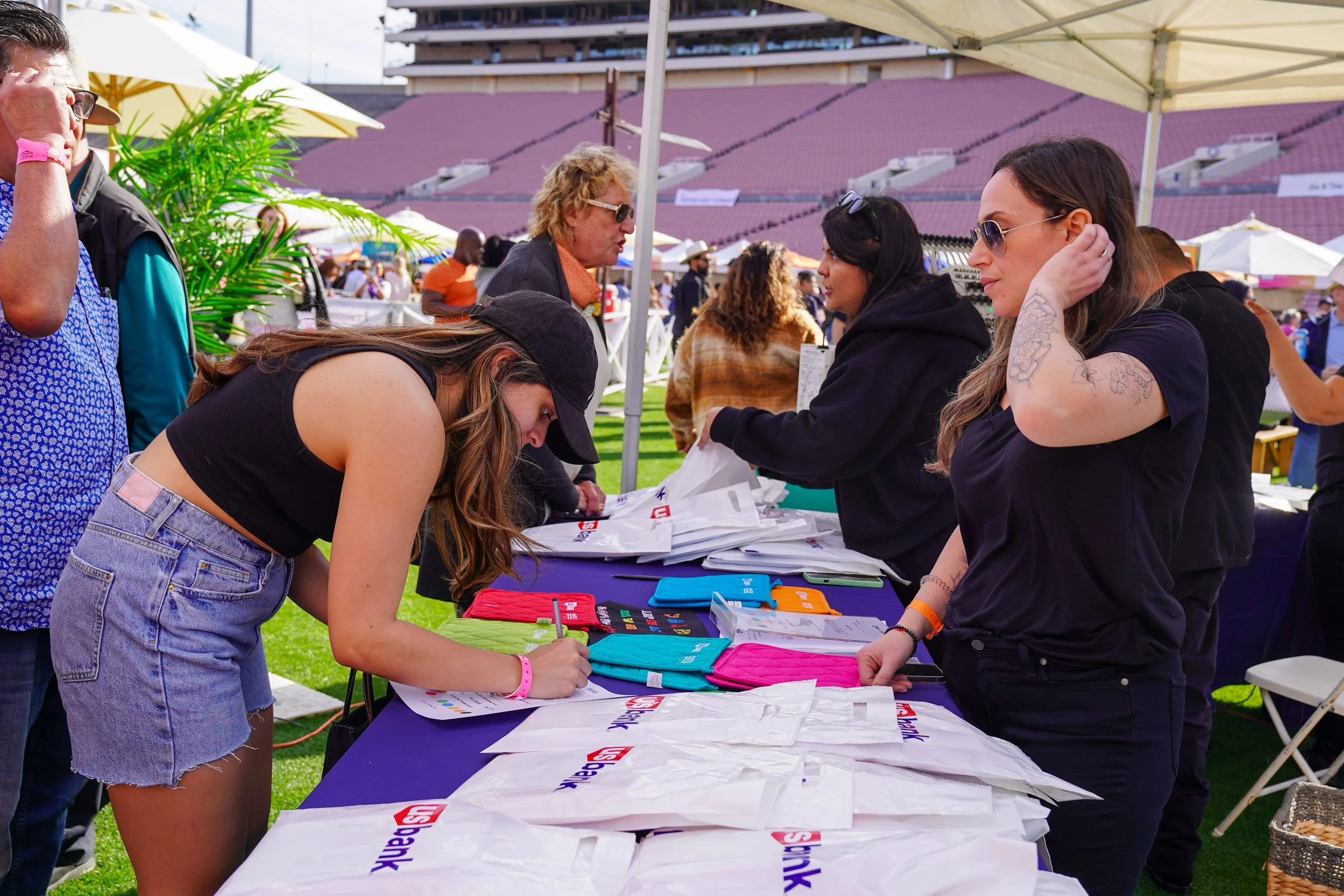 People at a table signing up at Masters of Taste, with bags and colorful items on the table.