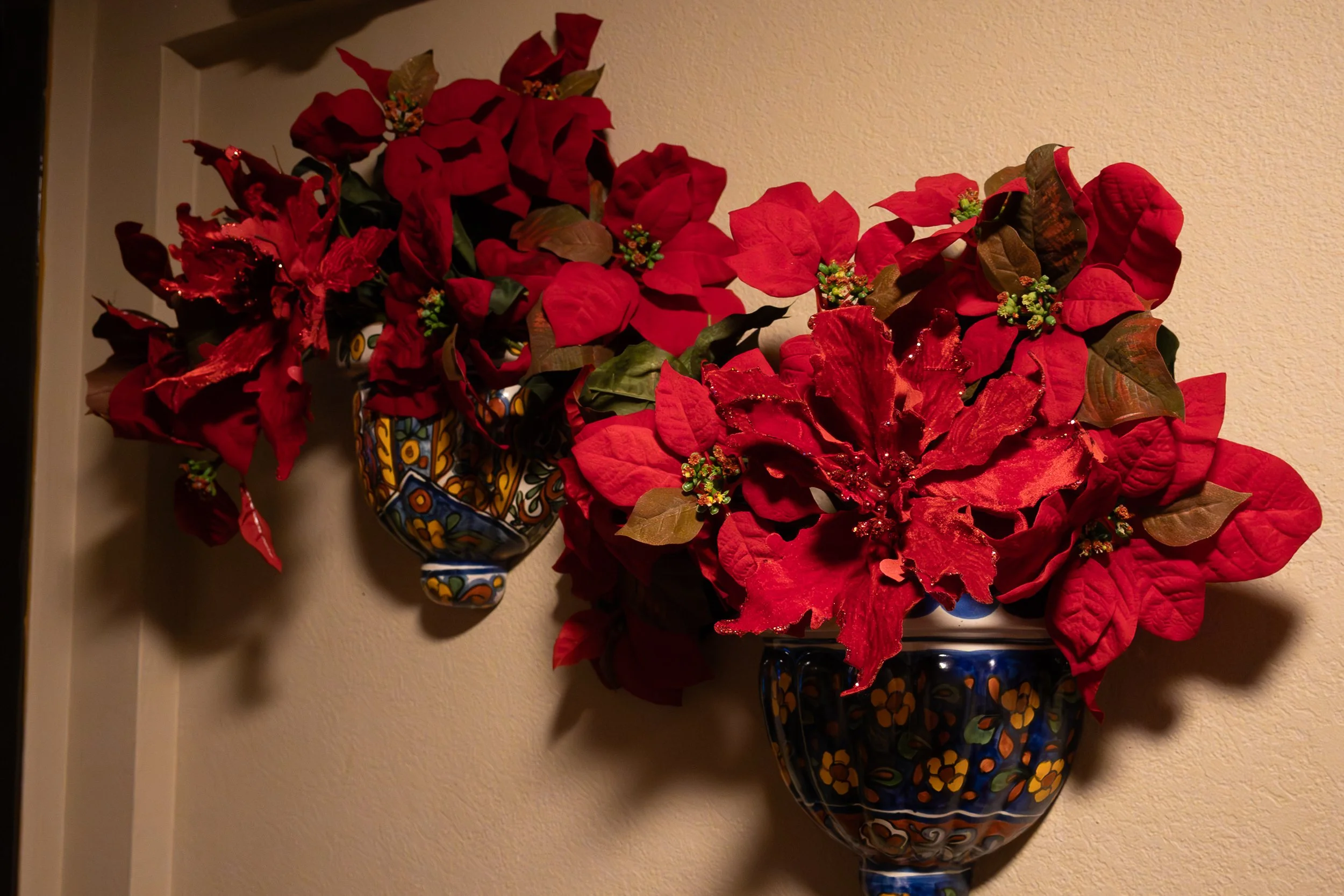 Decorative wall-mounted vases with red poinsettia flowers and green leaves in a home interior.