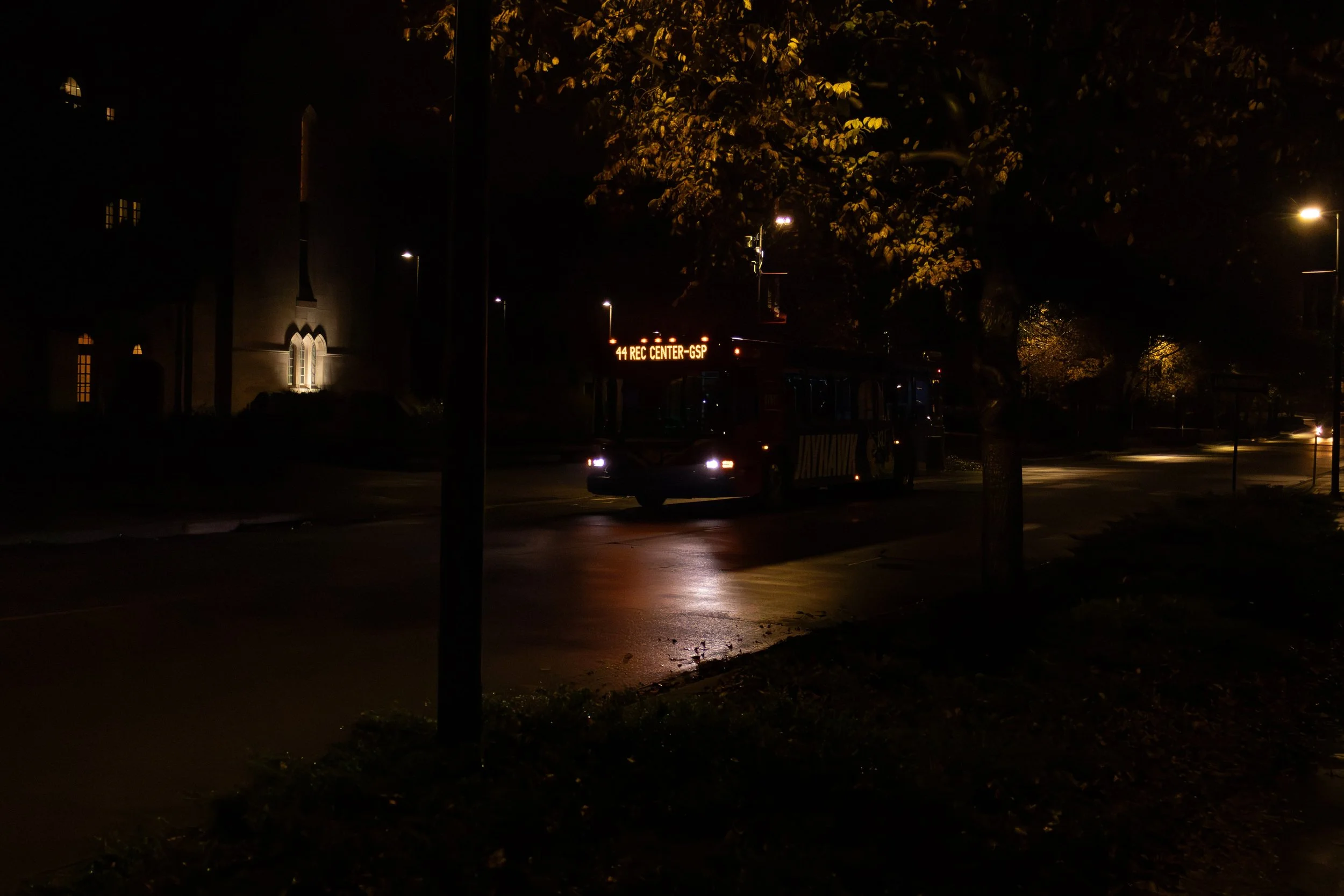 A bus traveling at night on a wet road with an illuminated sign reading '44 REC CENTER-GSP'.