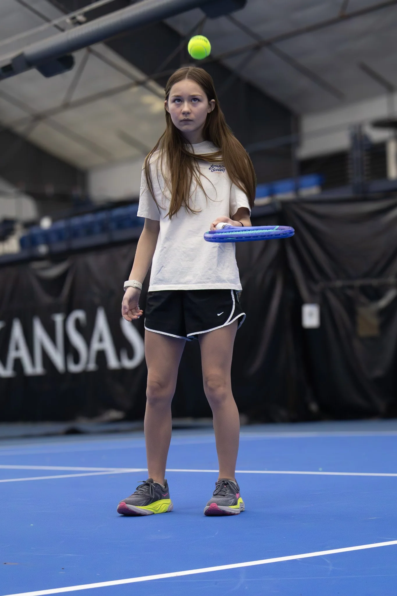 A young girl playing tennis indoors, holding a racket, preparing to hit a tennis ball.
