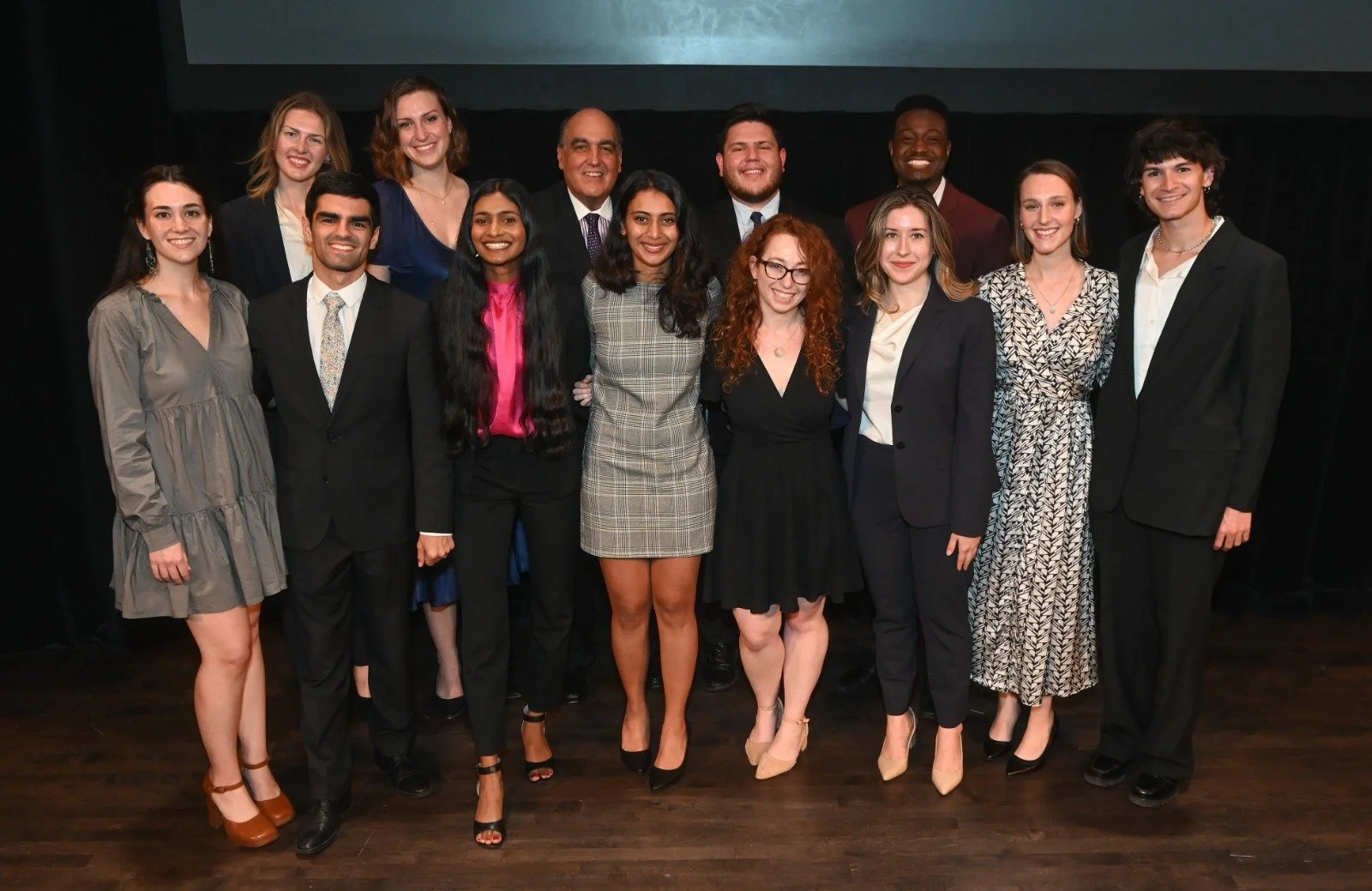 Group of people dressed in formal and semi-formal attire standing on stage at an event or ceremony.