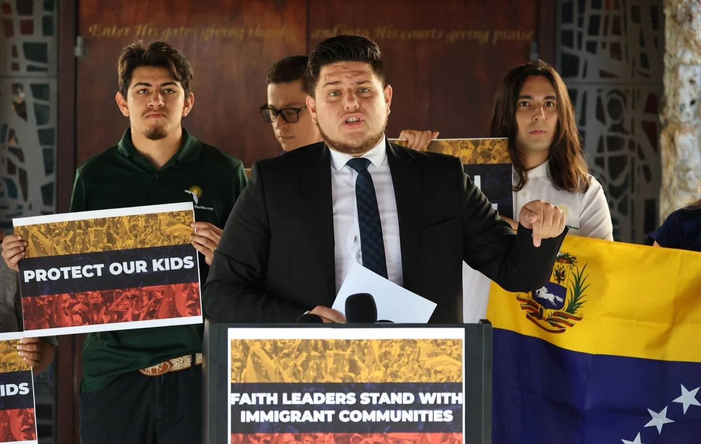 Group of young adults at a rally holding signs and a Venezuelan flag, advocating for immigrant communities and children protection.