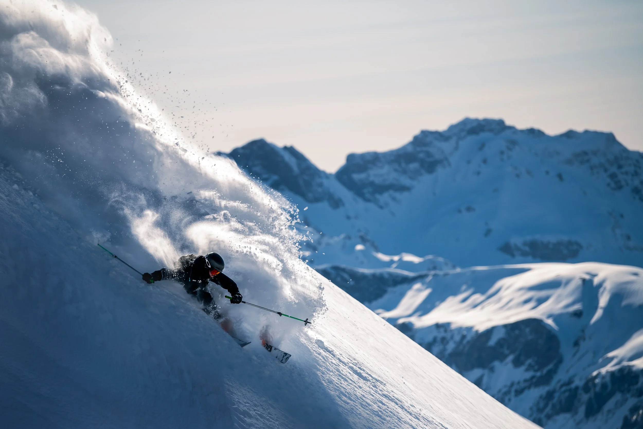 Sciatore che scende una ripida discesa di neve in montagna, con un paesaggio di montagne innevate sullo sfondo.