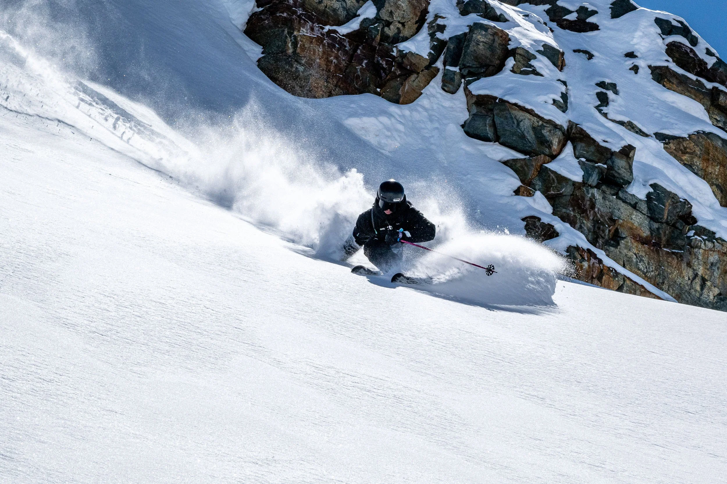 Una persona che scia sulla neve alta con uno sfondo di rocce innevate.