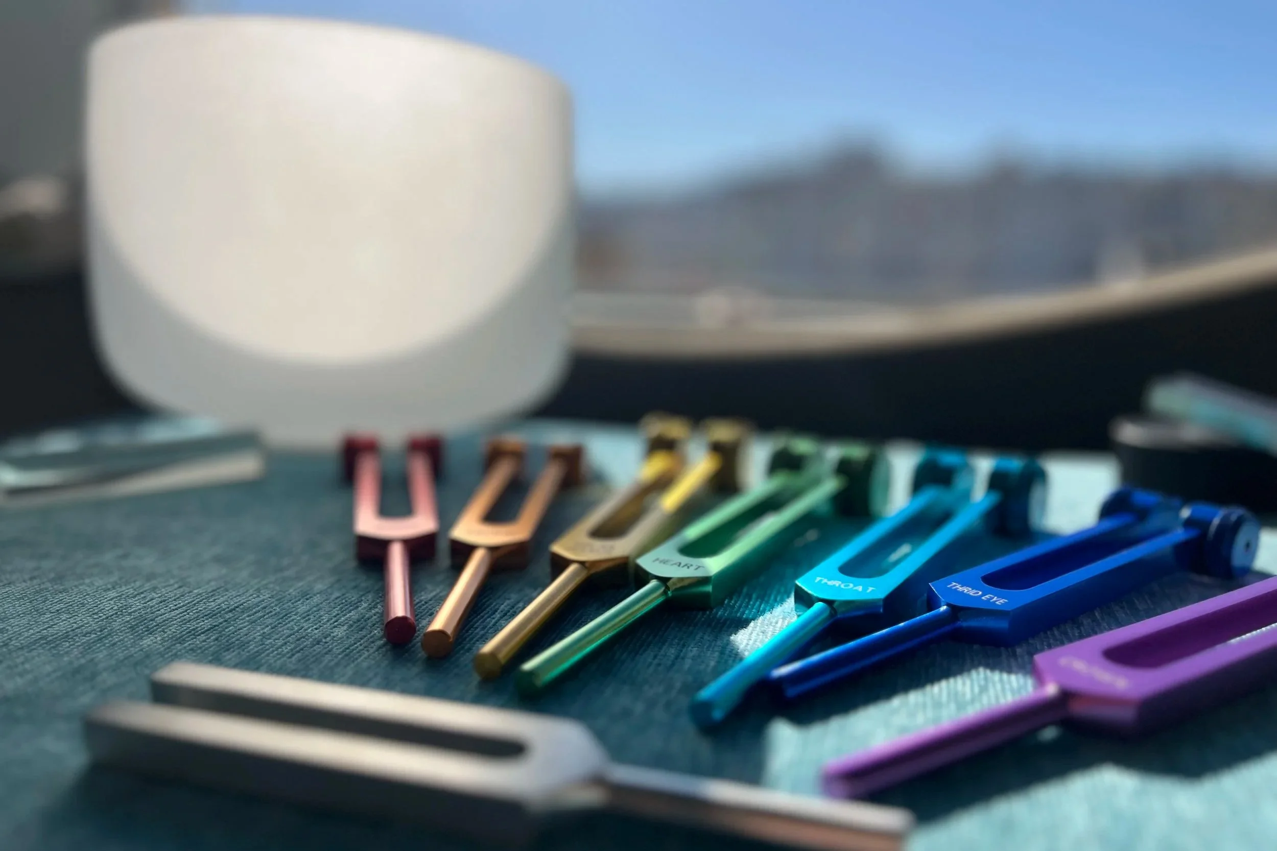 White singing bowl and colorful tuning forks used for sound healing and vibrational therapy.