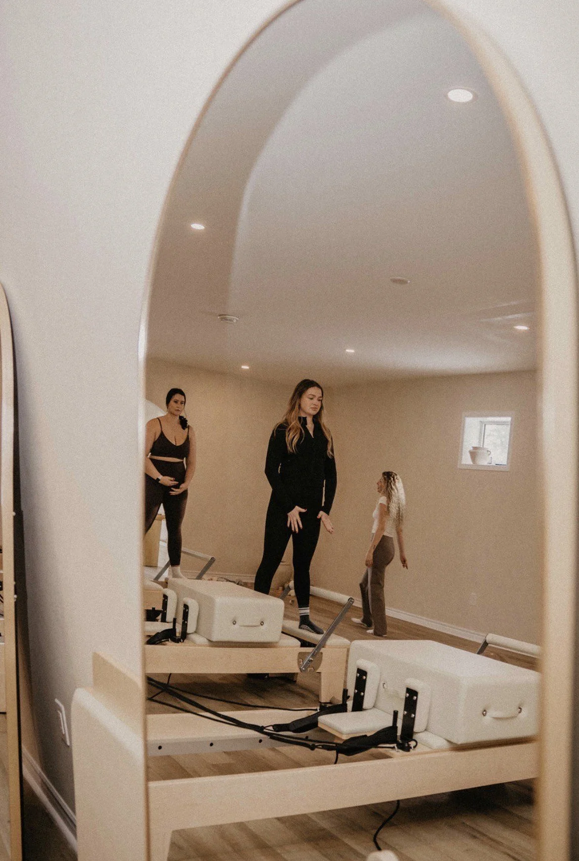 Three women practicing yoga in a studio, seen through a mirror.