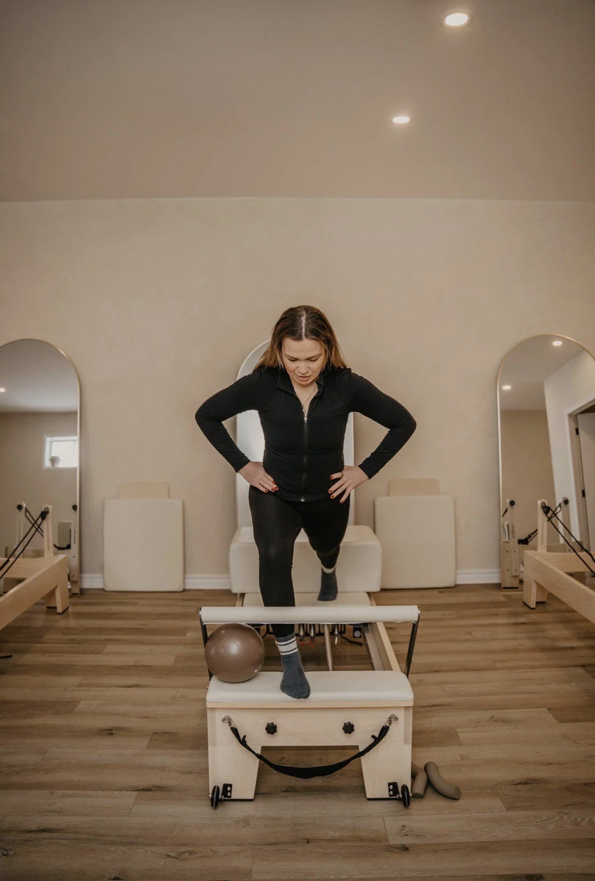 Woman exercising on a Pilates reformer machine in a studio.