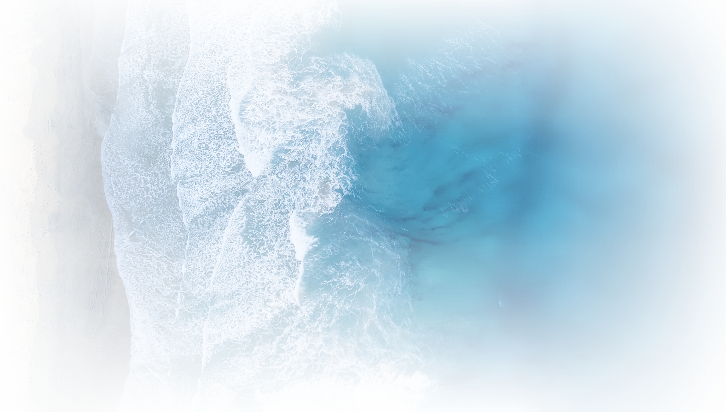 Aerial view of a beach with white sand and blue ocean waves crashing onto the shore.
