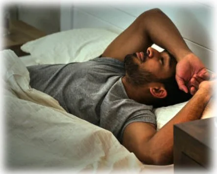 A traumatized man laying in bed during the day appears listless and afraid of facing reality.