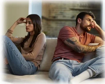 A man and woman facing away from each other while sitting on a sofa. They each each appear upset or in conflict.  Both are resting their heads on their hands.