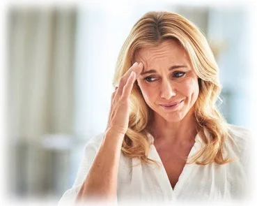 A woman with blonde hair holding her head and appearing worried or in pain.