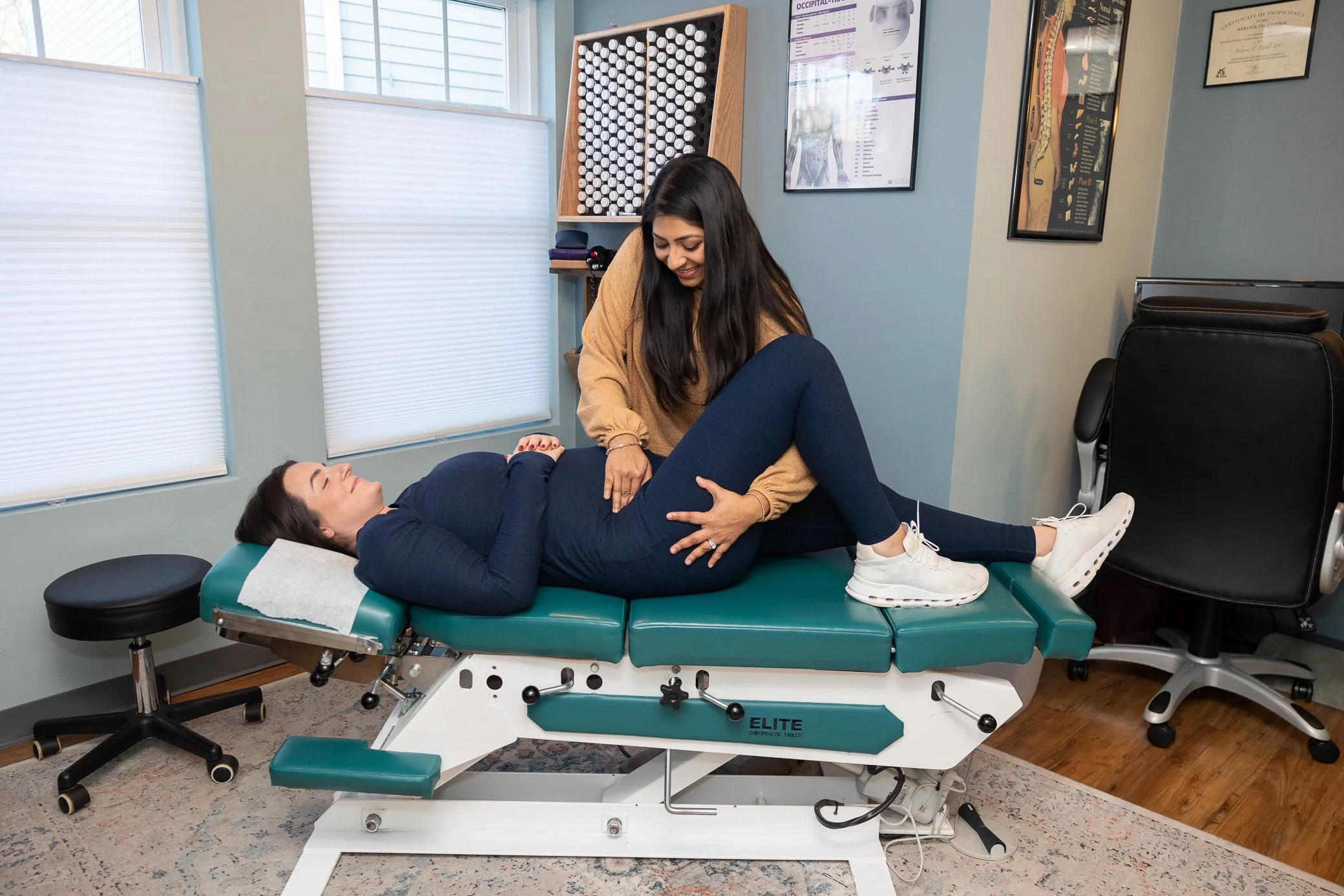 Dr. Shivani, a chiropractor, performing an adjustment on a pregnant female patient lying on an examination table in a medical office.