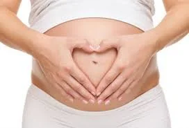 Close-up of a woman's belly with hands forming a heart shape over the stomach