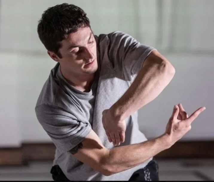 Young man in a gray t-shirt making a dance or hip-hop move with his arms crossed and fingers extended.