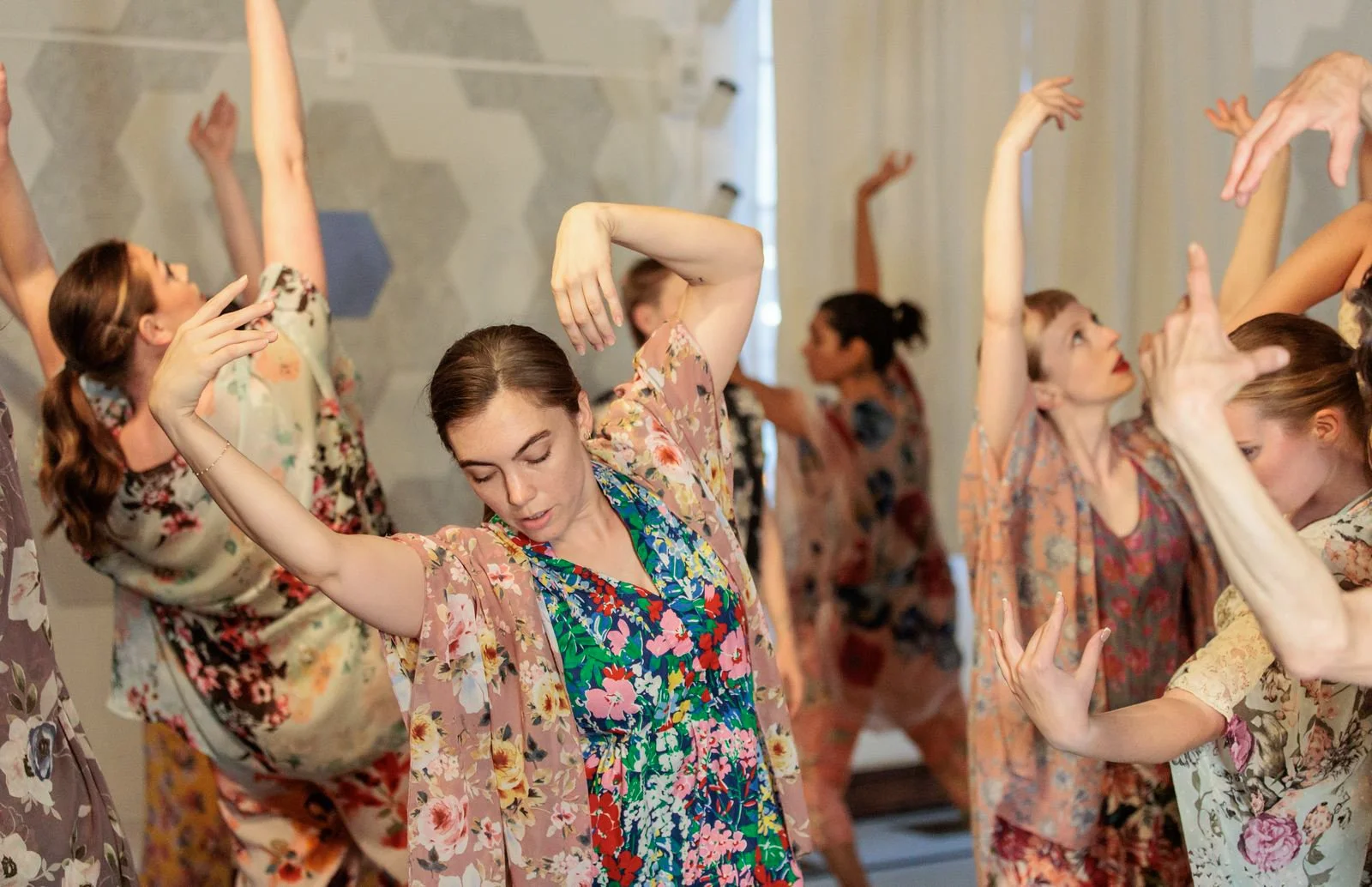 Group of women in floral robes practicing dance poses in a studio.