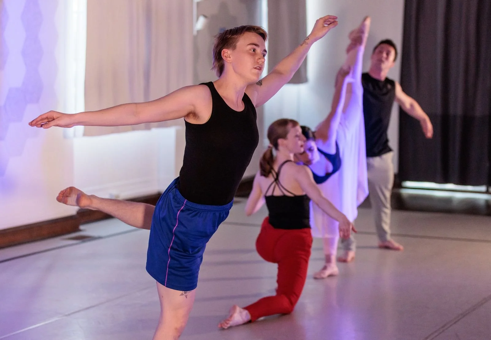 Four dancers strike a contemporary pose in a dramatically lit dance studio.