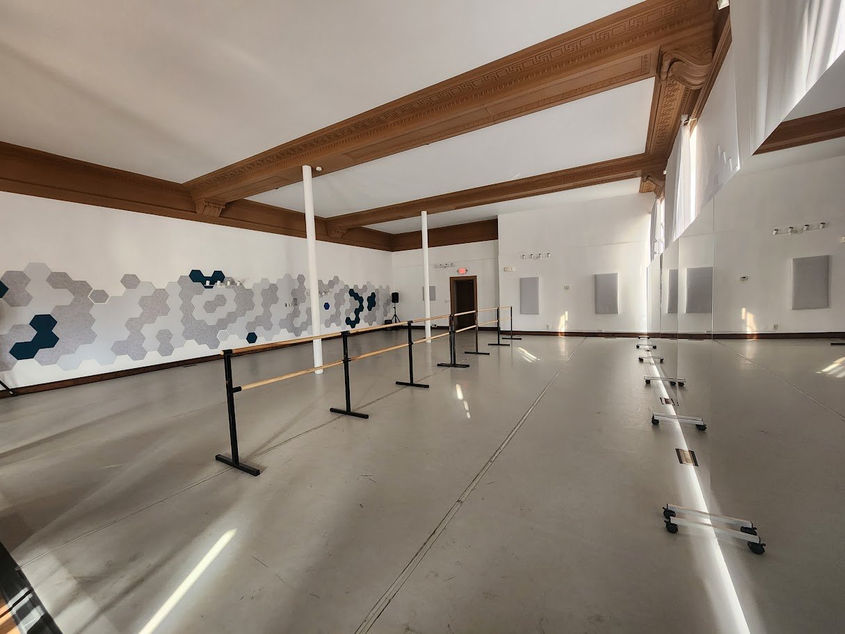 Empty dance studio with ballet barre, mirrors, and patterned wall art.