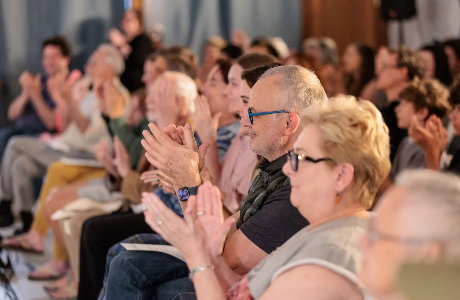 People sitting in a church or auditorium, clapping and smiling, attending a joyful event.