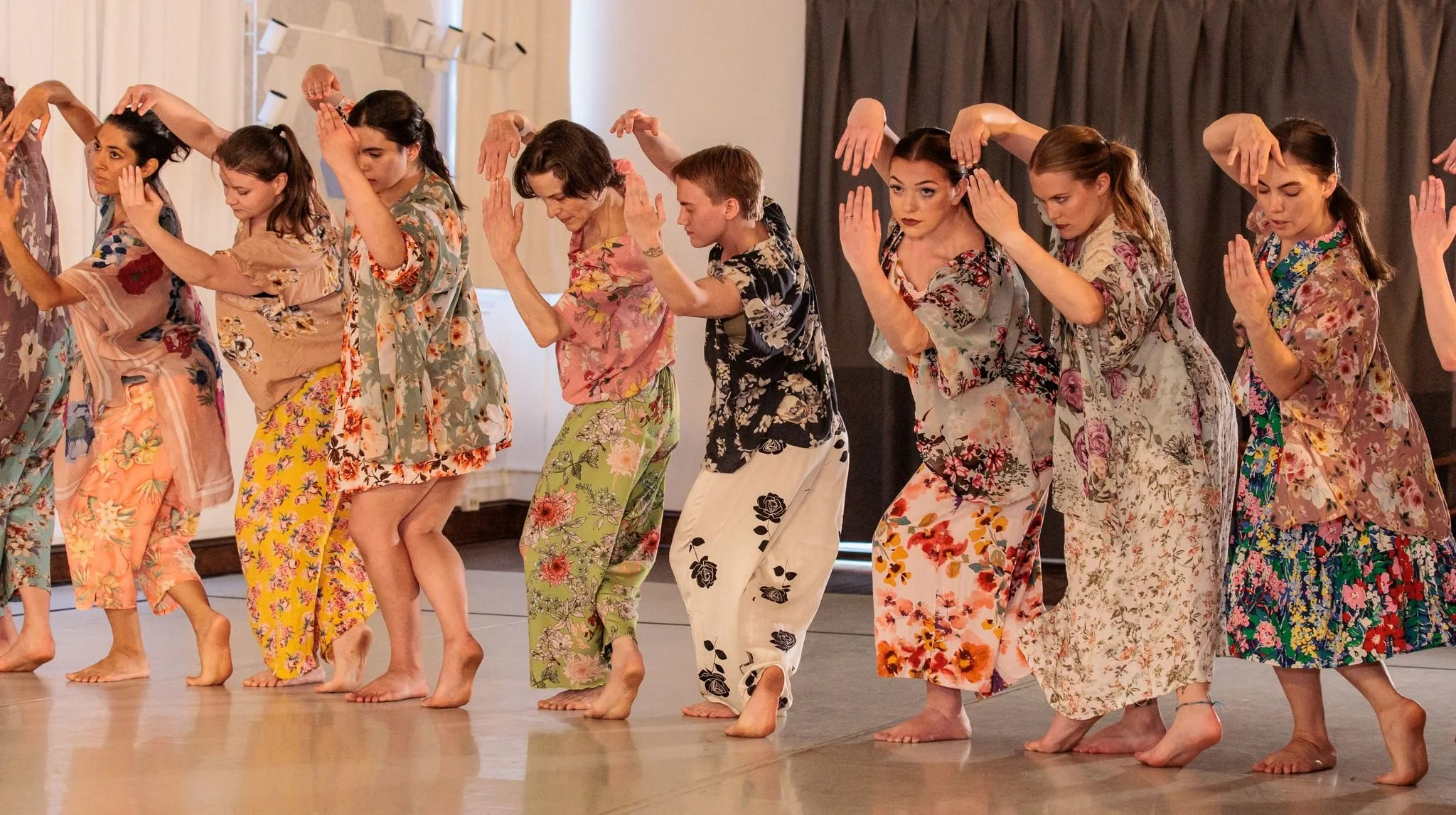 A group of women and a boy wearing vibrant floral pajamas in various contrasting colors, barefoot, performing in HDC's white box studio.