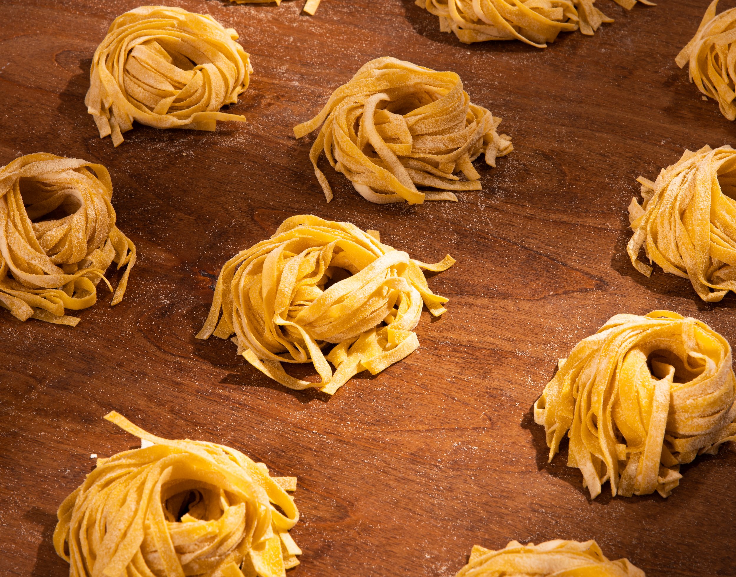 Multiple nests of uncooked fettuccine pasta on a wooden surface