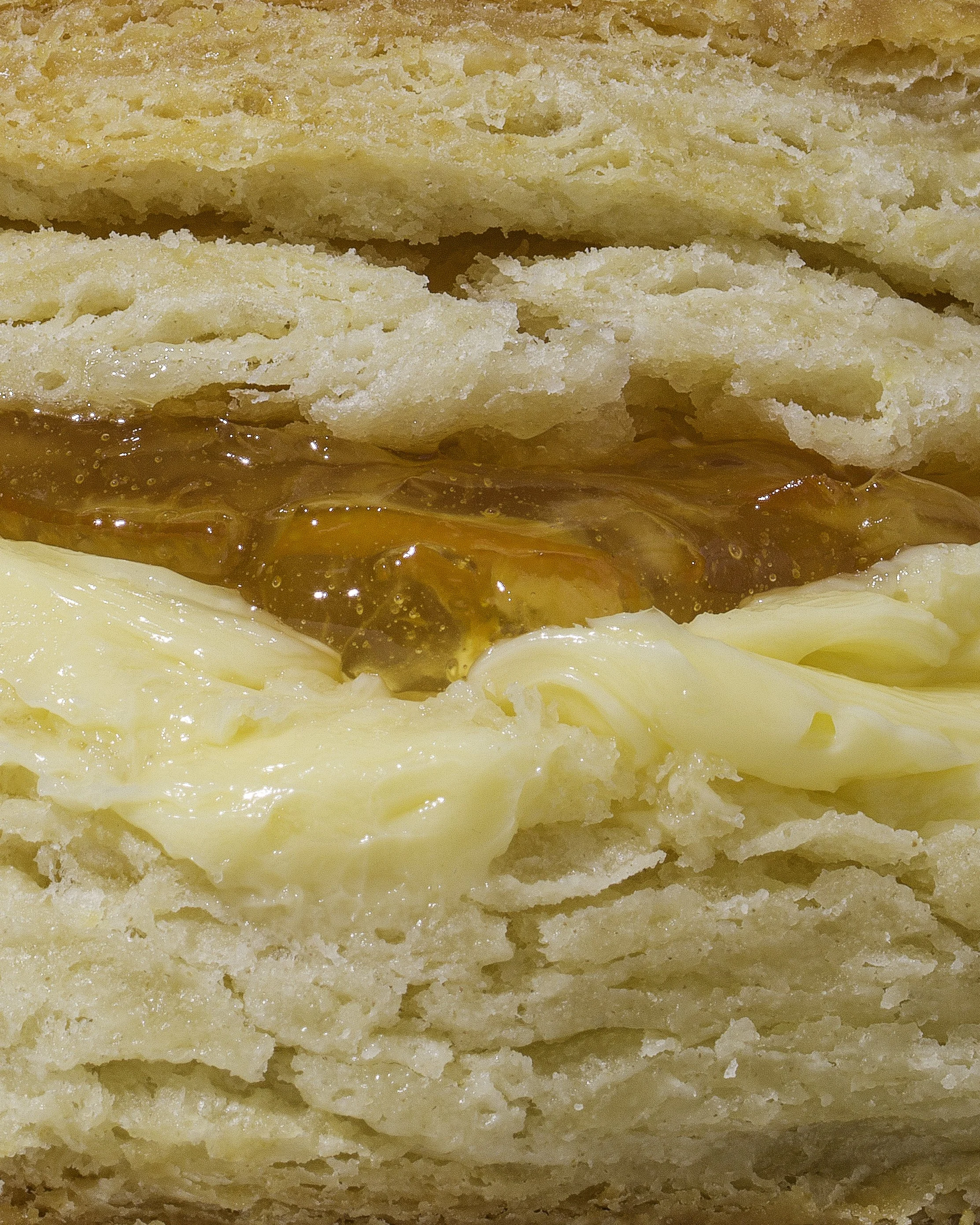 Close-up of a buttermilk biscuit with flaky layers, orange marmalade, and butter.