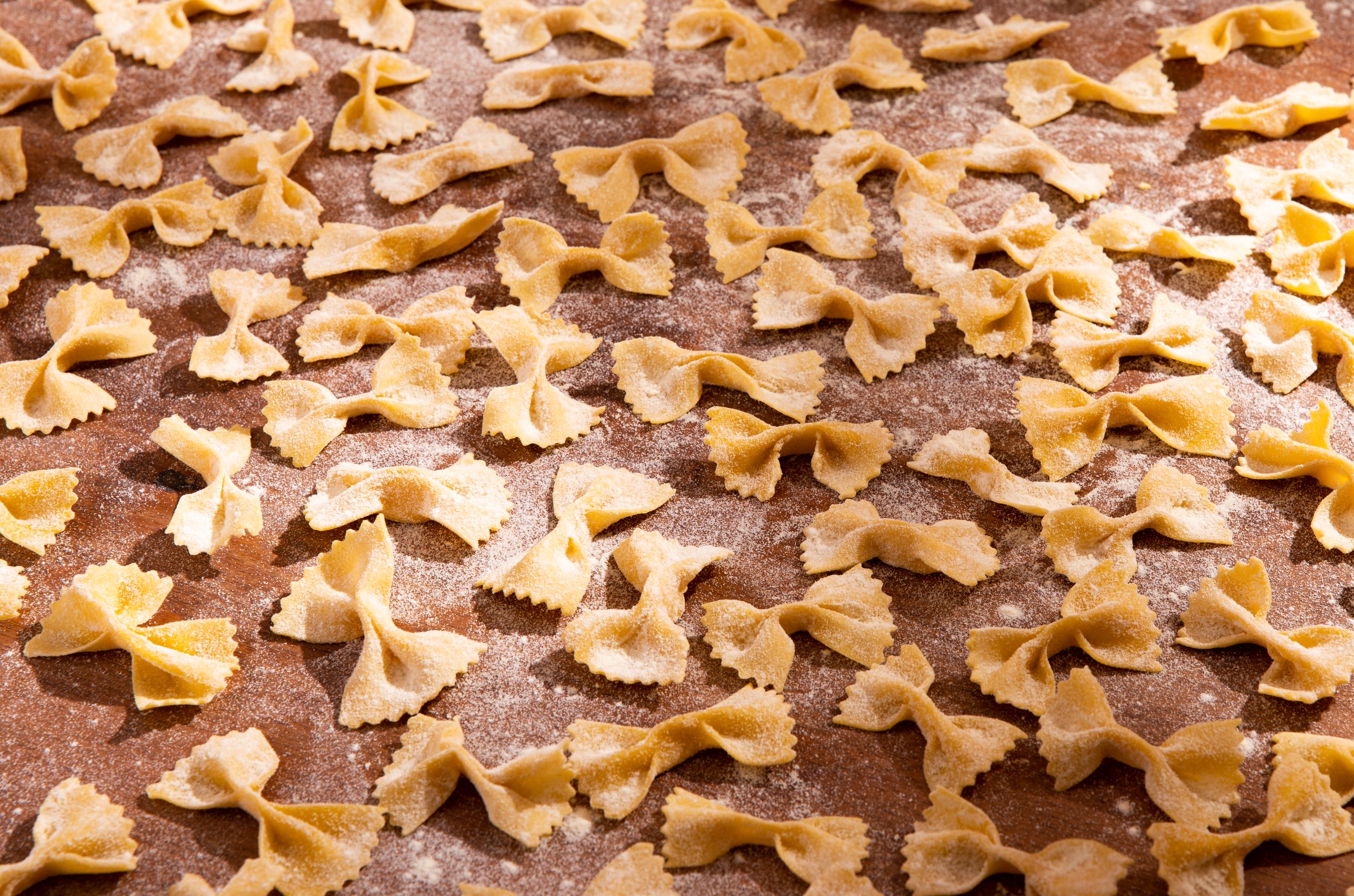 Uncooked bowtie pasta scattered on a floured surface.