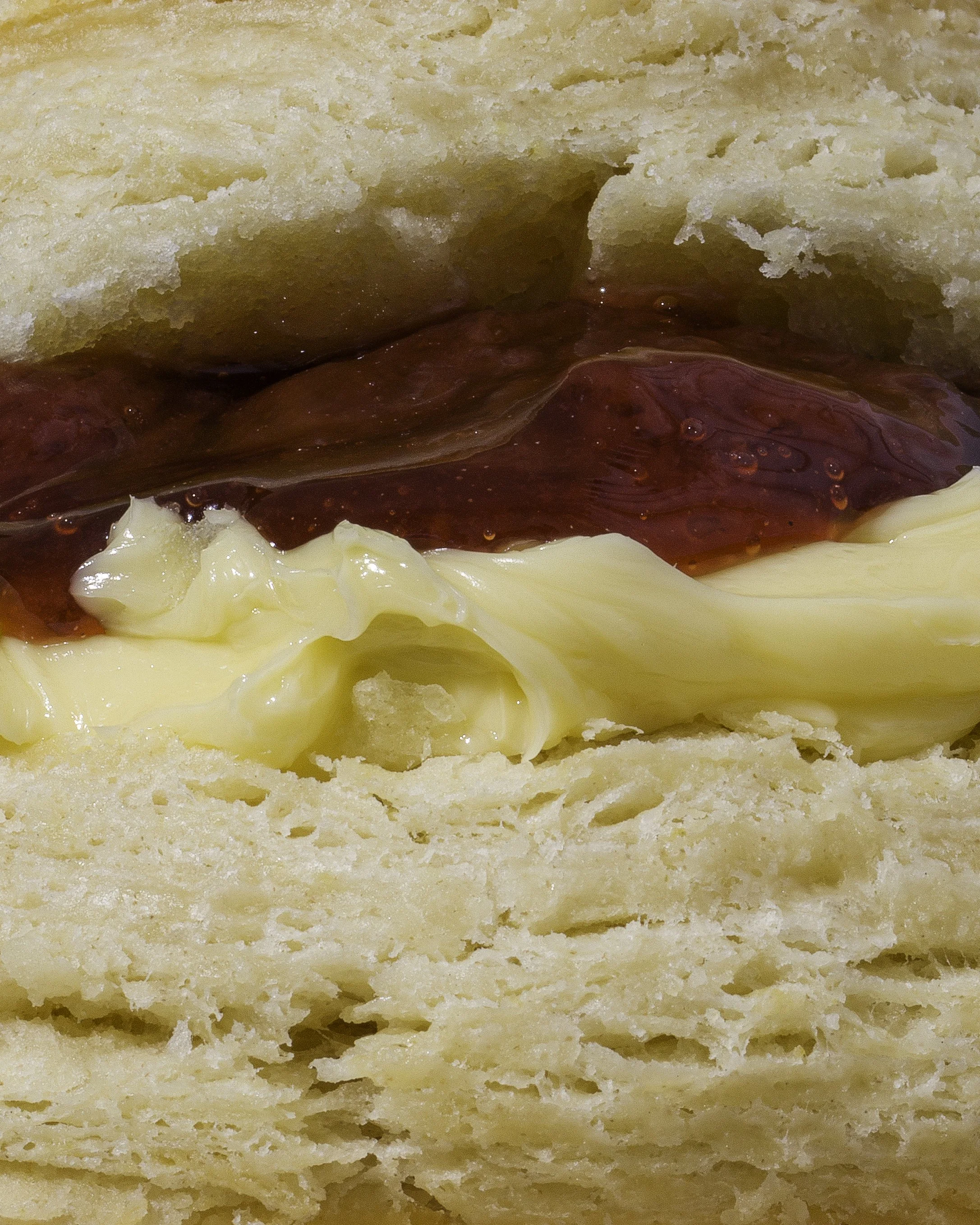 Close-up of a biscuit top and bottom, filled with butter and strawberry fruit jam.