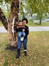 Woman carrying a child on her back outdoors near a tree in a park