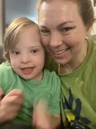 A woman smiling next to a young girl, both wearing green shirts, close-up selfie.