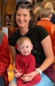 Woman smiling with a young girl in a red outfit sitting on her lap in a bookstore or library setting.