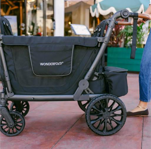 Black Wonderfold stroller on a sidewalk outdoor with a person standing nearby.