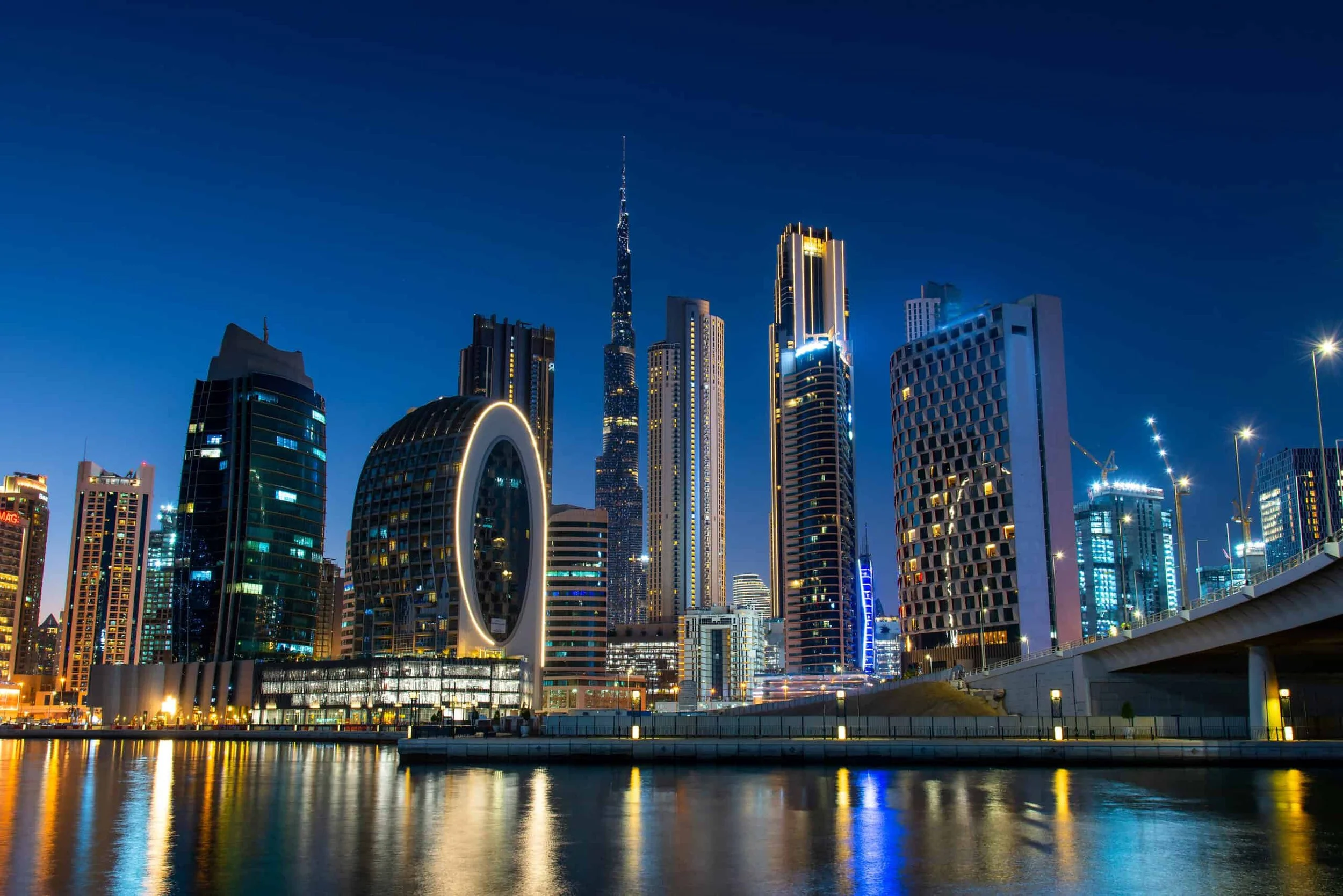 Night view of Dubai's downtown skyline with illuminated skyscrapers and reflections on water.