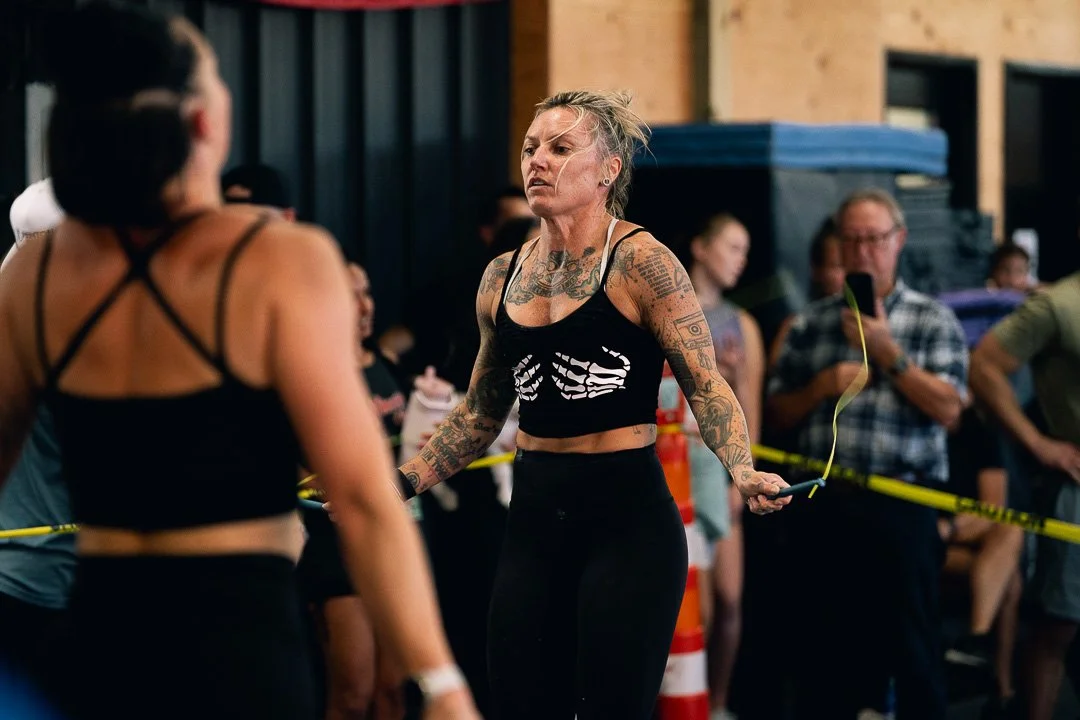 A woman with tattoos skipping rope at a gym or fitness event, surrounded by onlookers.