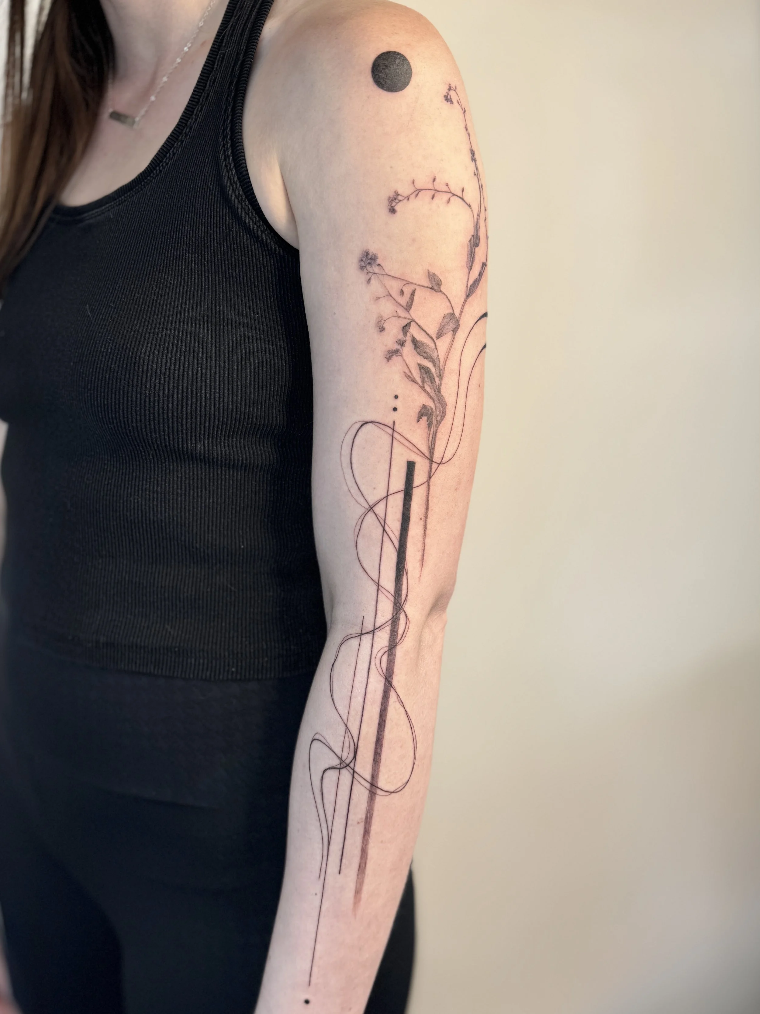 Tattoo of a microrealistic forget me not, a solid black dot near the shoulder, and a fineline abstract lines and geometry from a Reach series. Full sleeve abstract concept tattoo