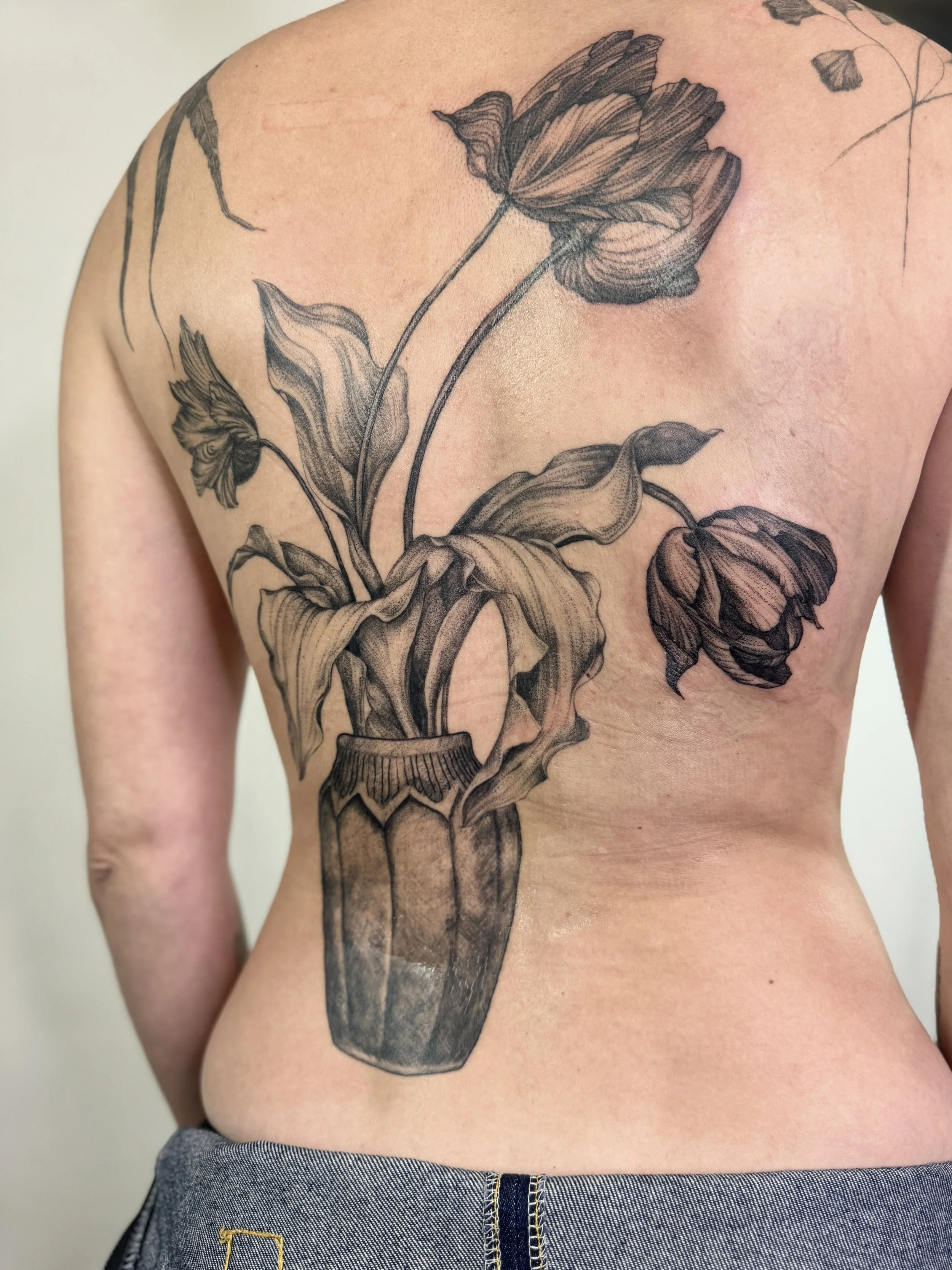 Black and gray botanical tattoo of a vase with wilted tulips on a person's back.  fine line tattoo Vancouver by Petra Zakoucka