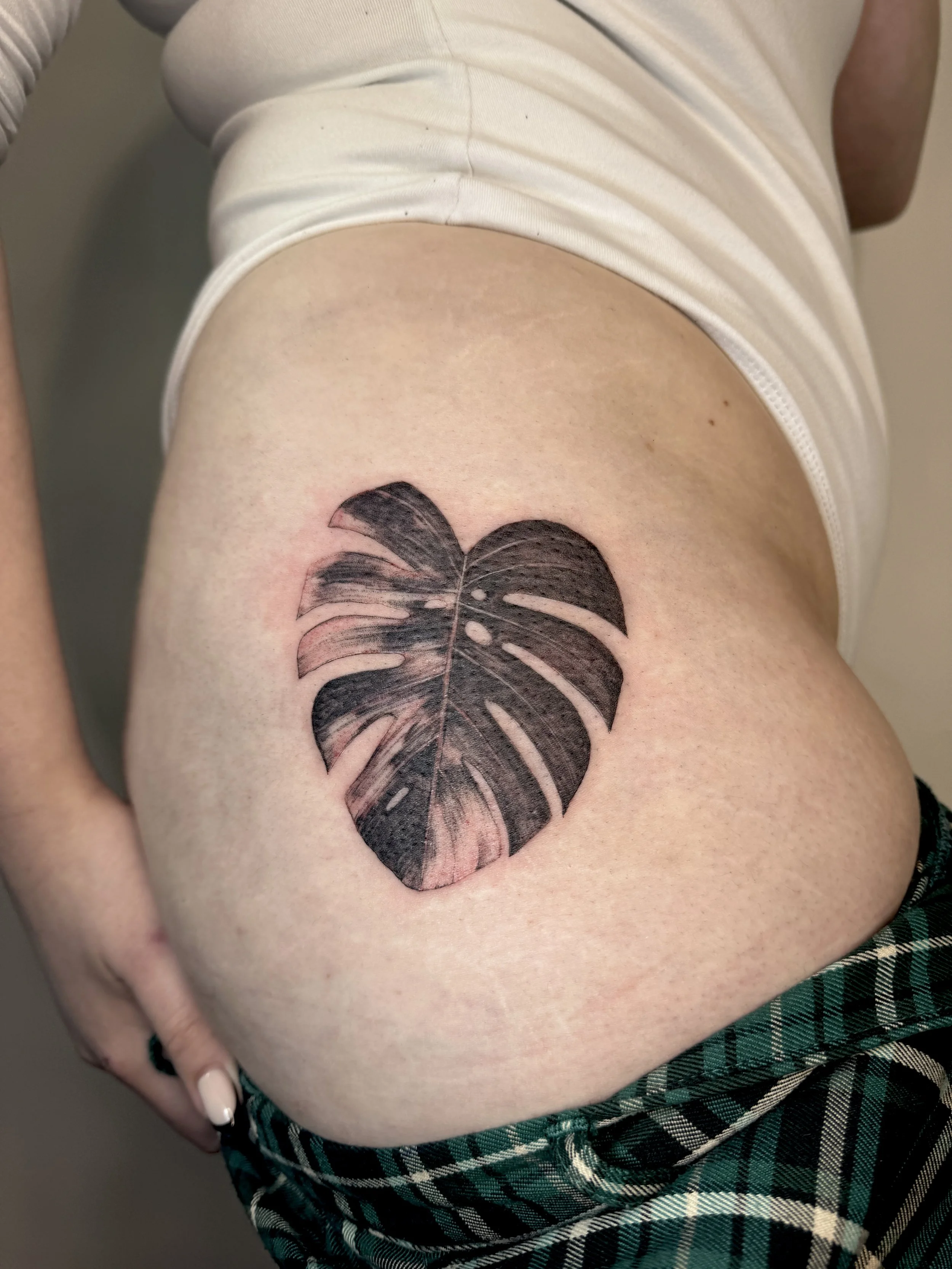 Tattoo of a black microrealistic Monstera leaf on person's upper thigh. Botanical tattoo created using real leaf imprint, fine line tattoo artist in Vancouver