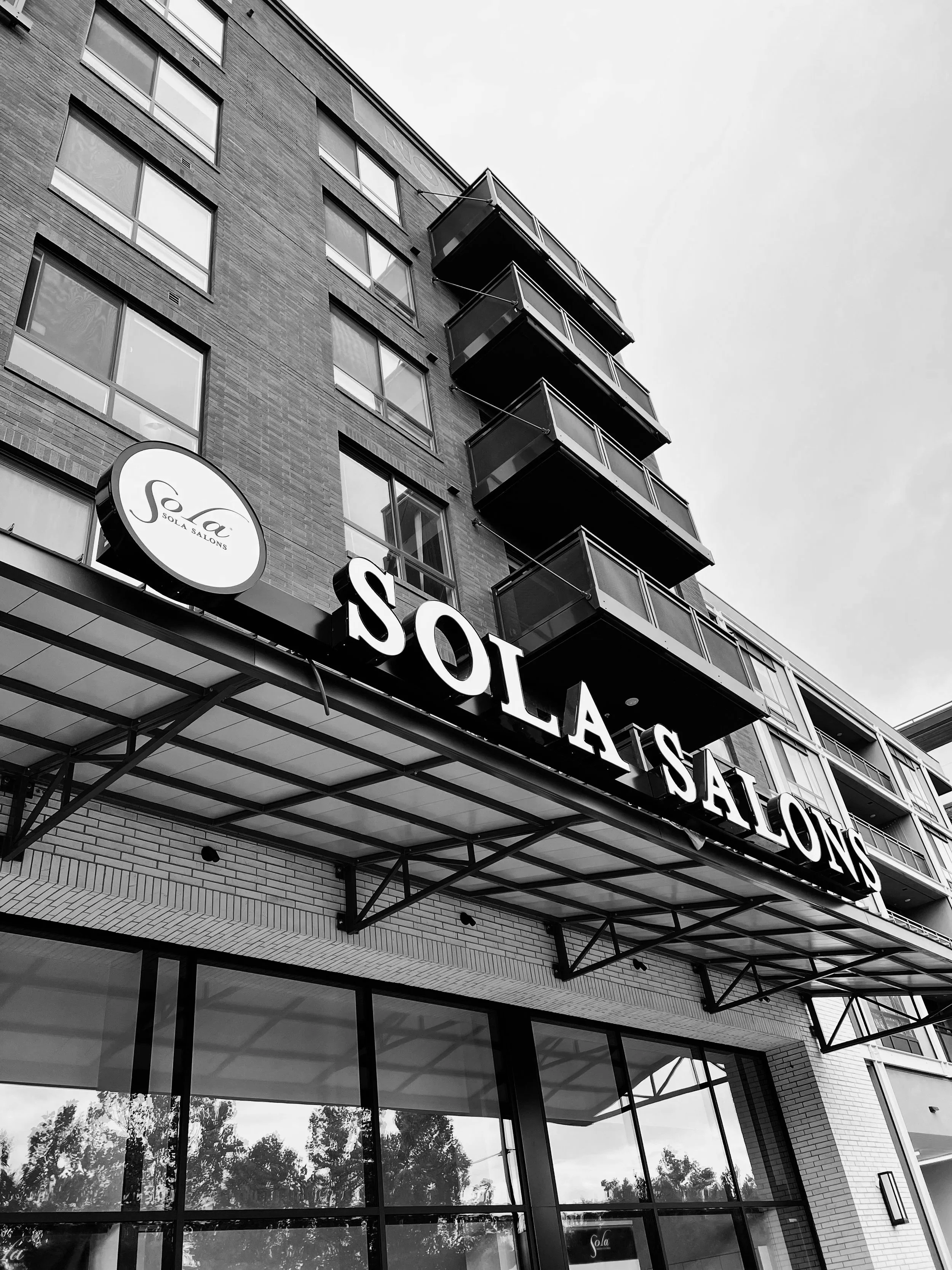 Black and white photo of a multi-story building with a sign reading 'Solà Salons' above the entrance and several balconies on the upper floors.