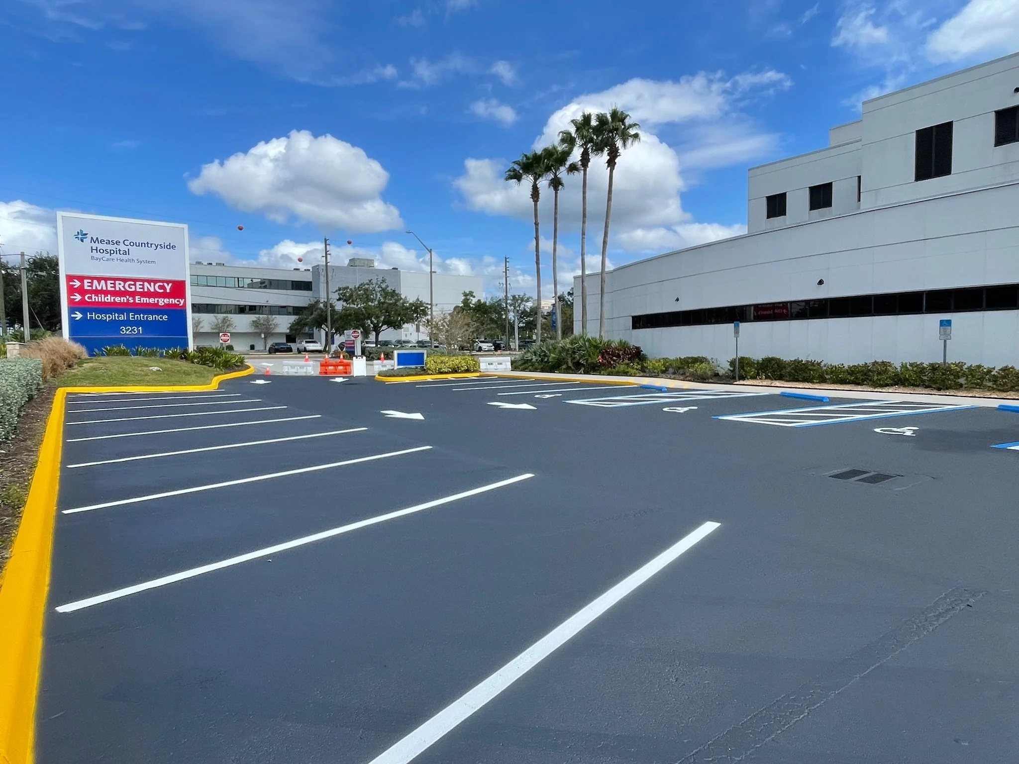 Freshly redone hospital parking lot of Mease Countryside Hospital with clear blue sky, palm trees, and hospital building in the background.