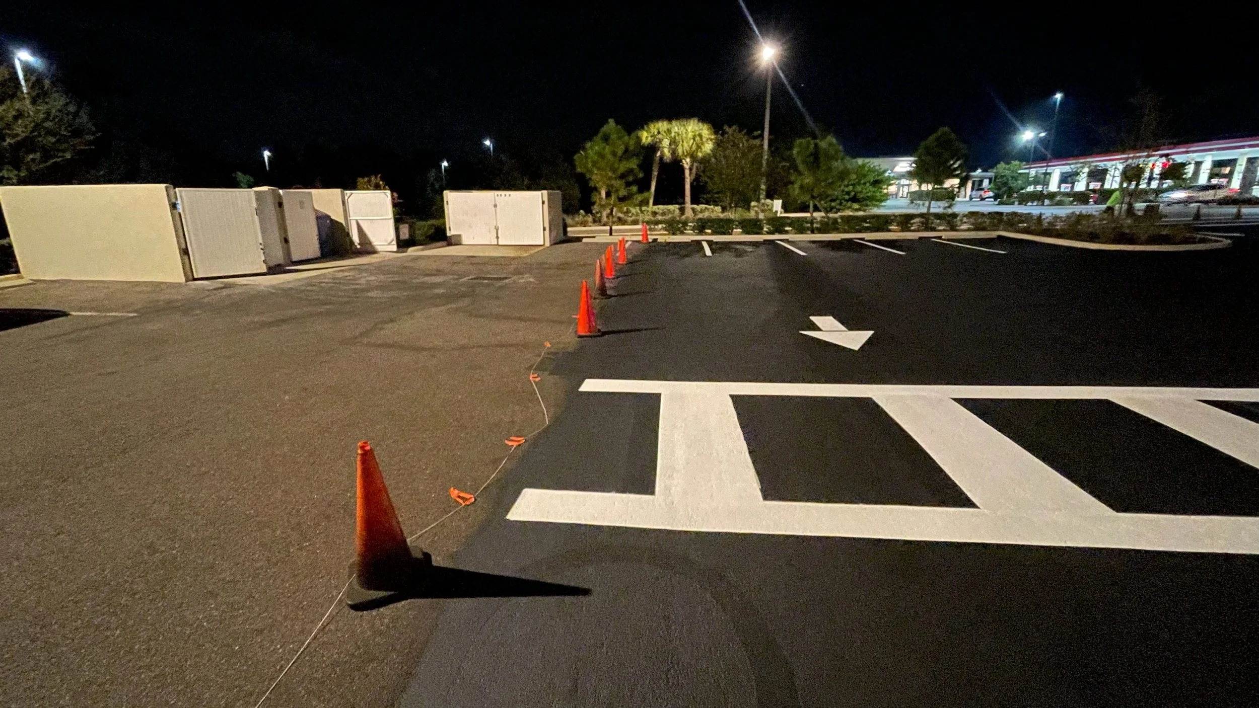 Empty parking lot at night with orange traffic cones, freshly painted parking space lines, and a large directional arrow painted on the pavement.