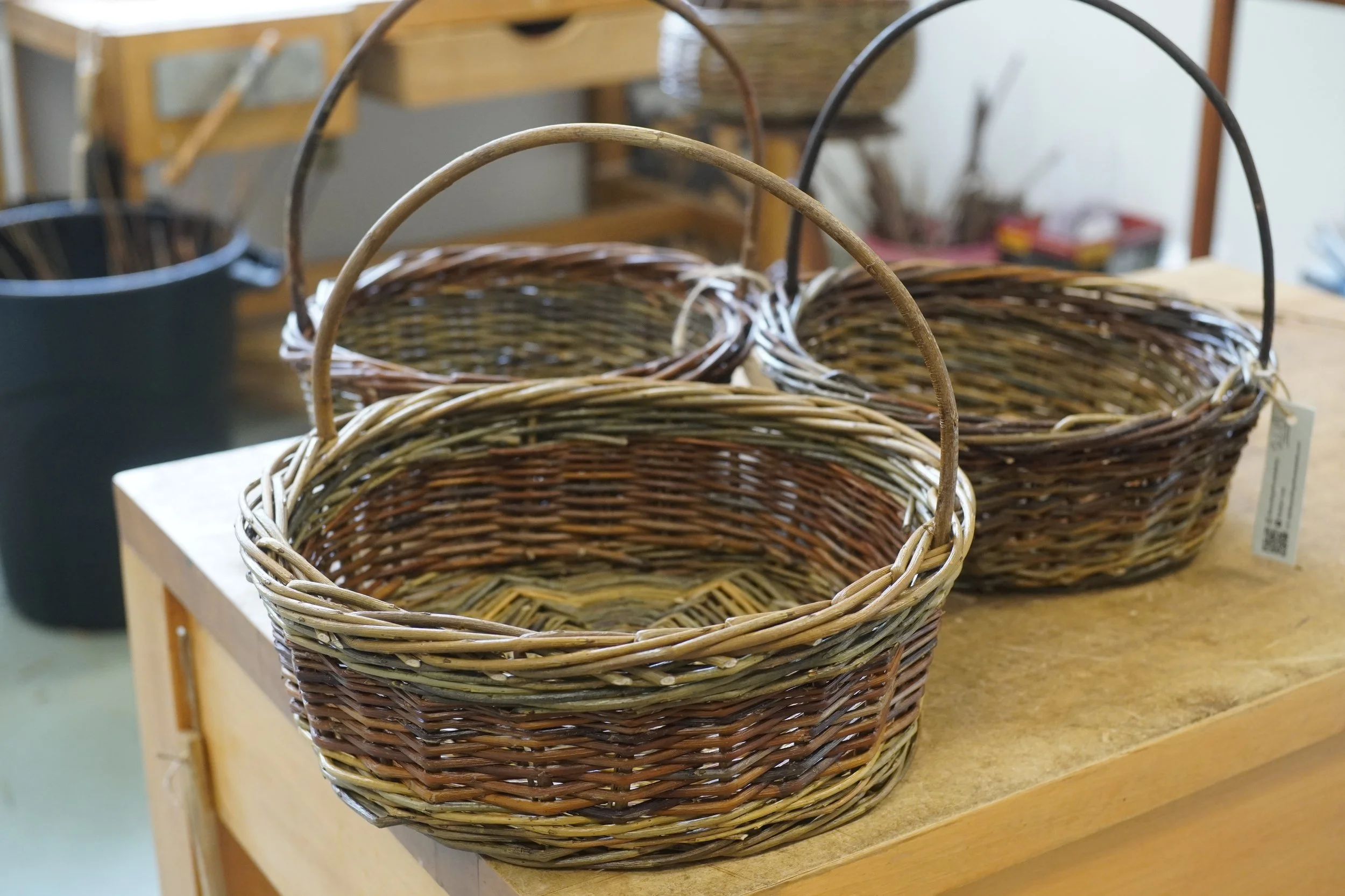 A display of empty woven wicker baskets of various sizes on a wooden table in a store or craft shop.
