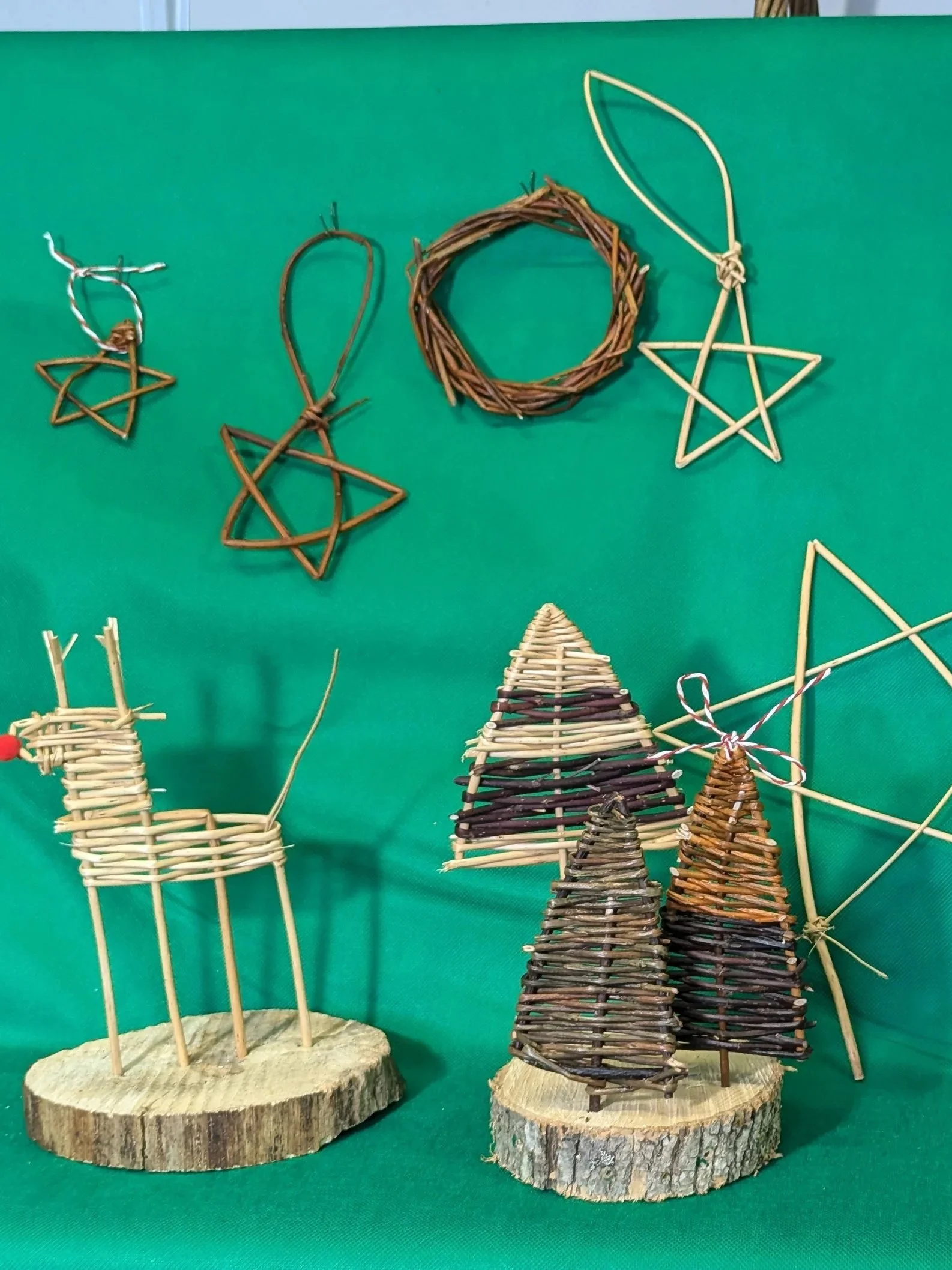 Wooden and willow Christmas decorations, including reindeer, Christmas trees, and stars displayed on a green background.