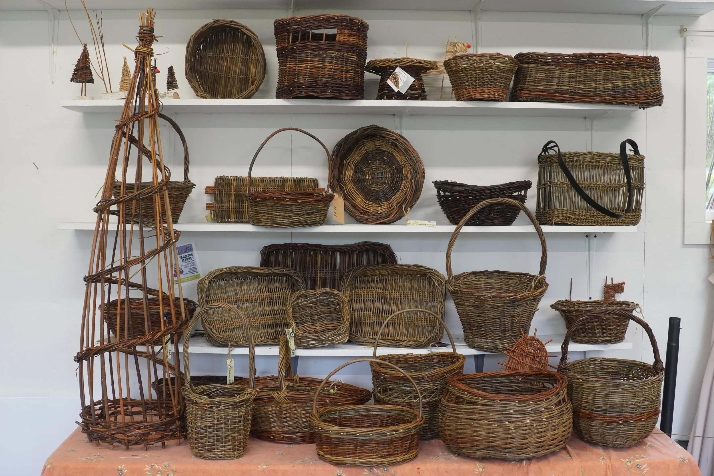 A display of woven baskets on white shelves and a table, with various shapes and sizes, made from natural materials. The scene appears to be in a craft or art store.