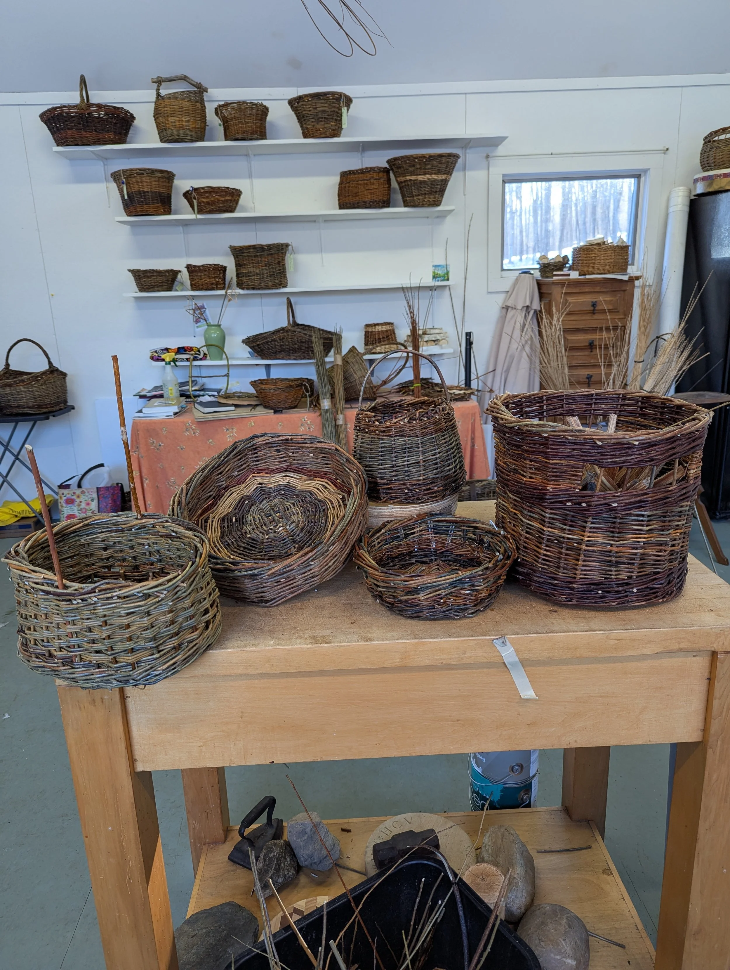Various handmade woven baskets displayed on a table and shelves in a craft workshop setting.