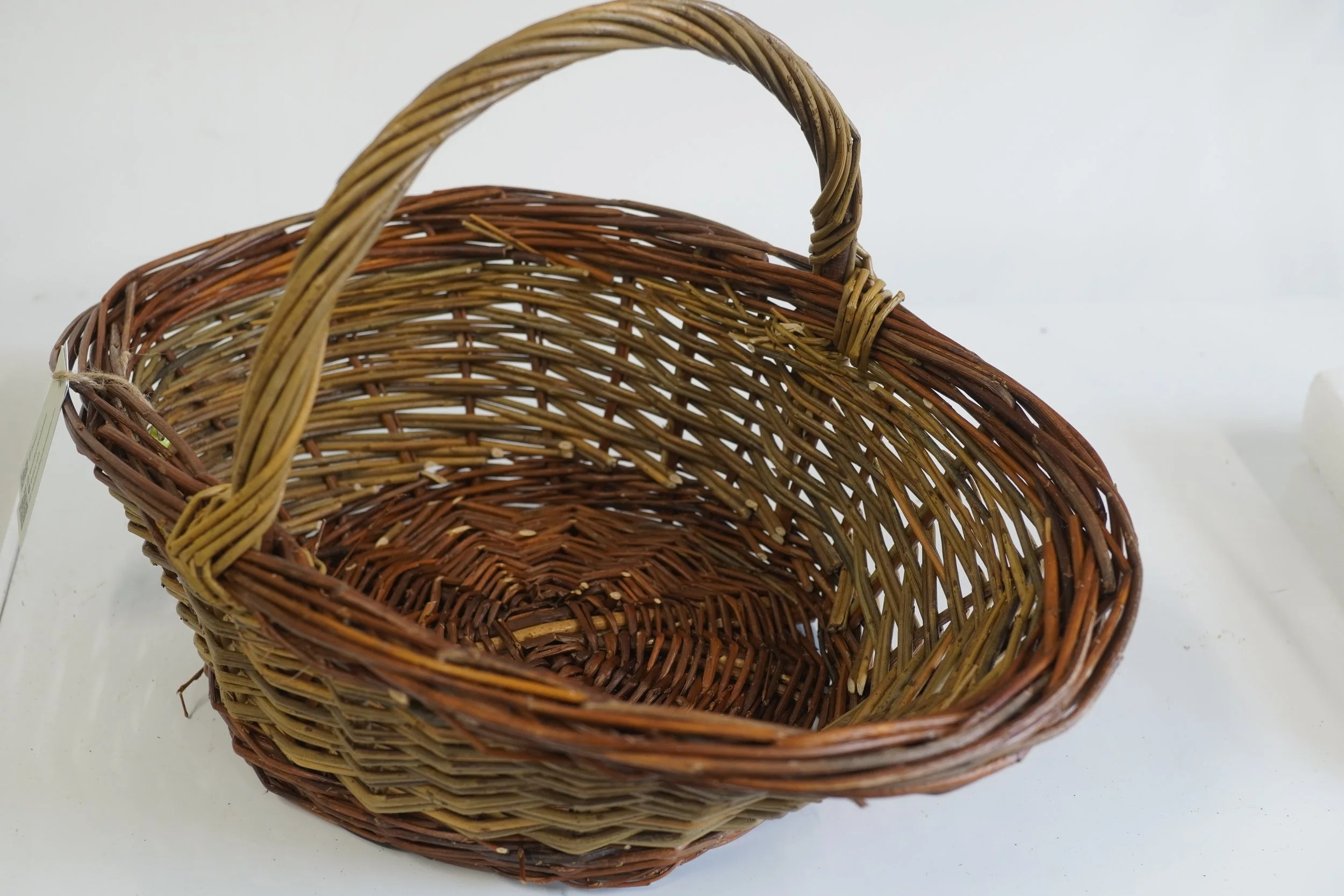 Three woven wicker baskets stacked inside each other, with the top basket having a handle, on a white surface against a plain background.